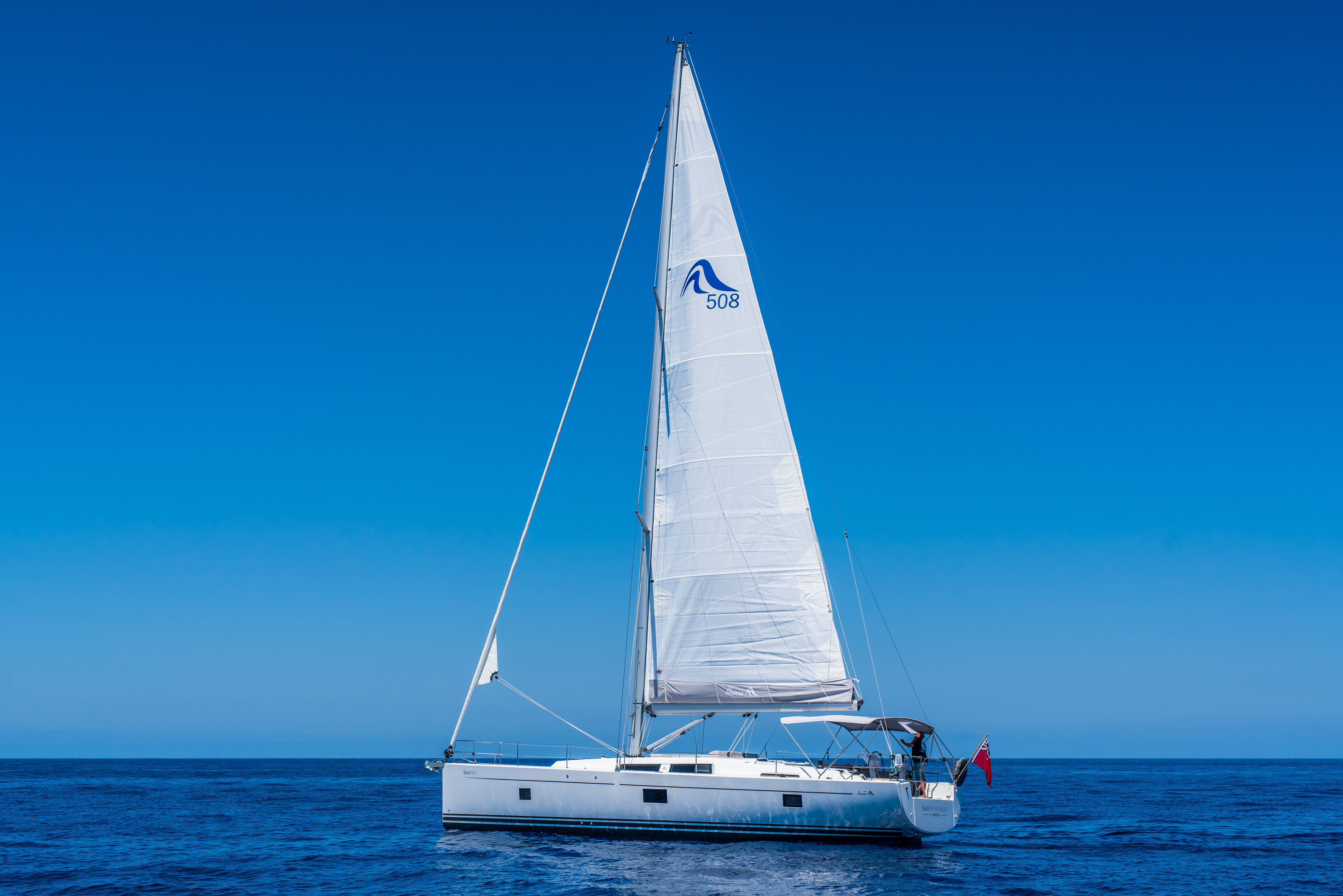 White sailing yacht on deep blue ocean with clear blue sky.