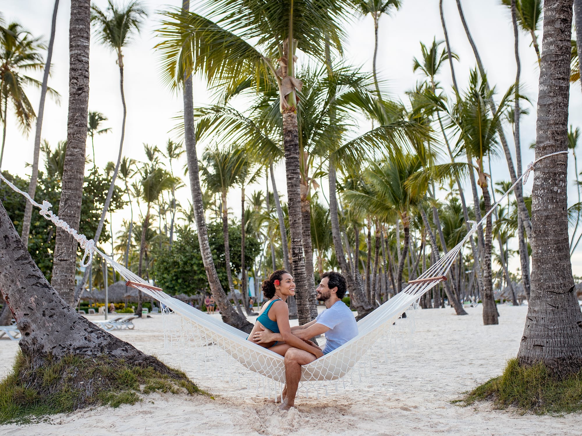 a man and woman sitting in a hammock on a beach