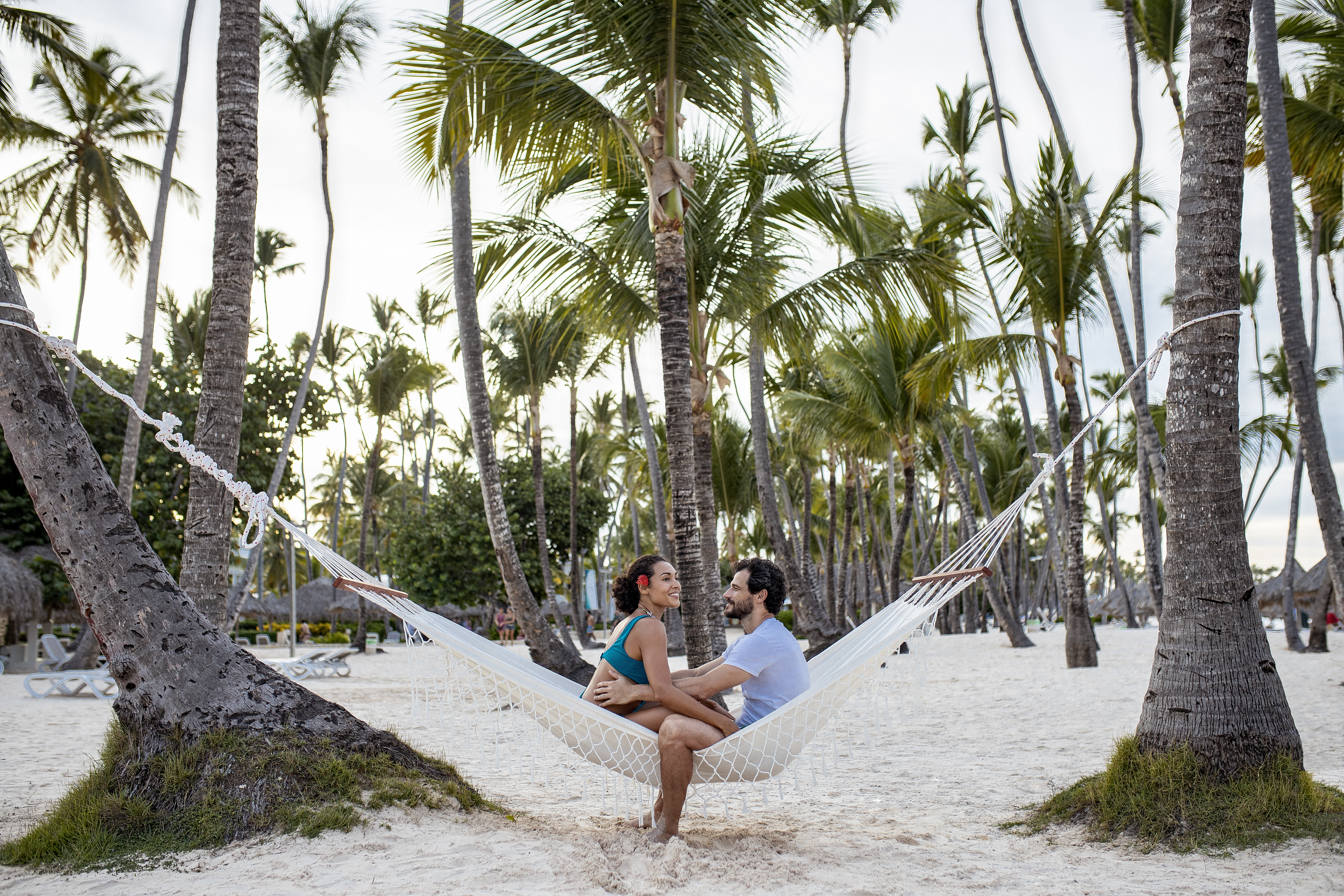 a man and woman sitting in a hammock on a beach