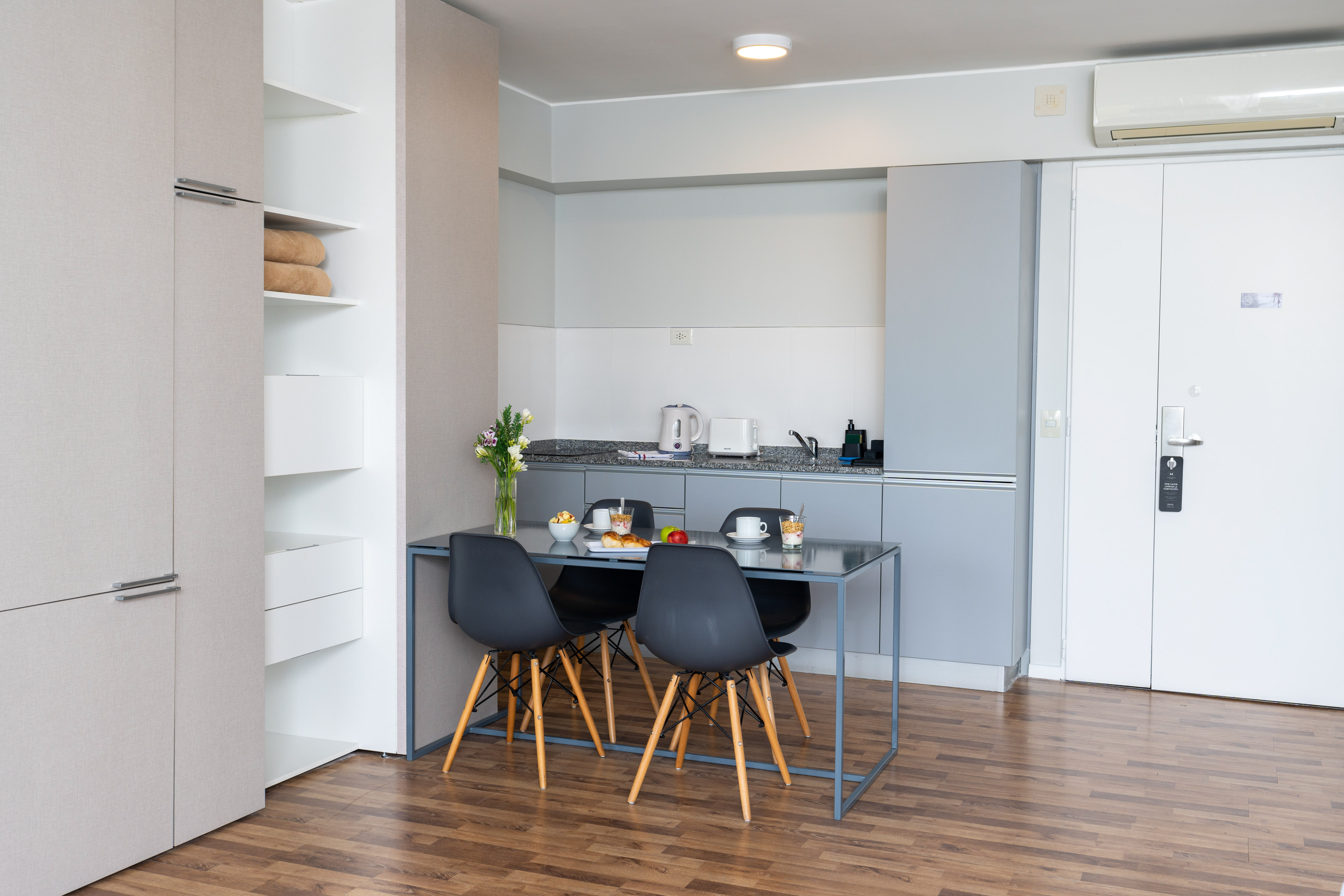 Modern studio apartment with kitchenette, dining table, and wood floor.