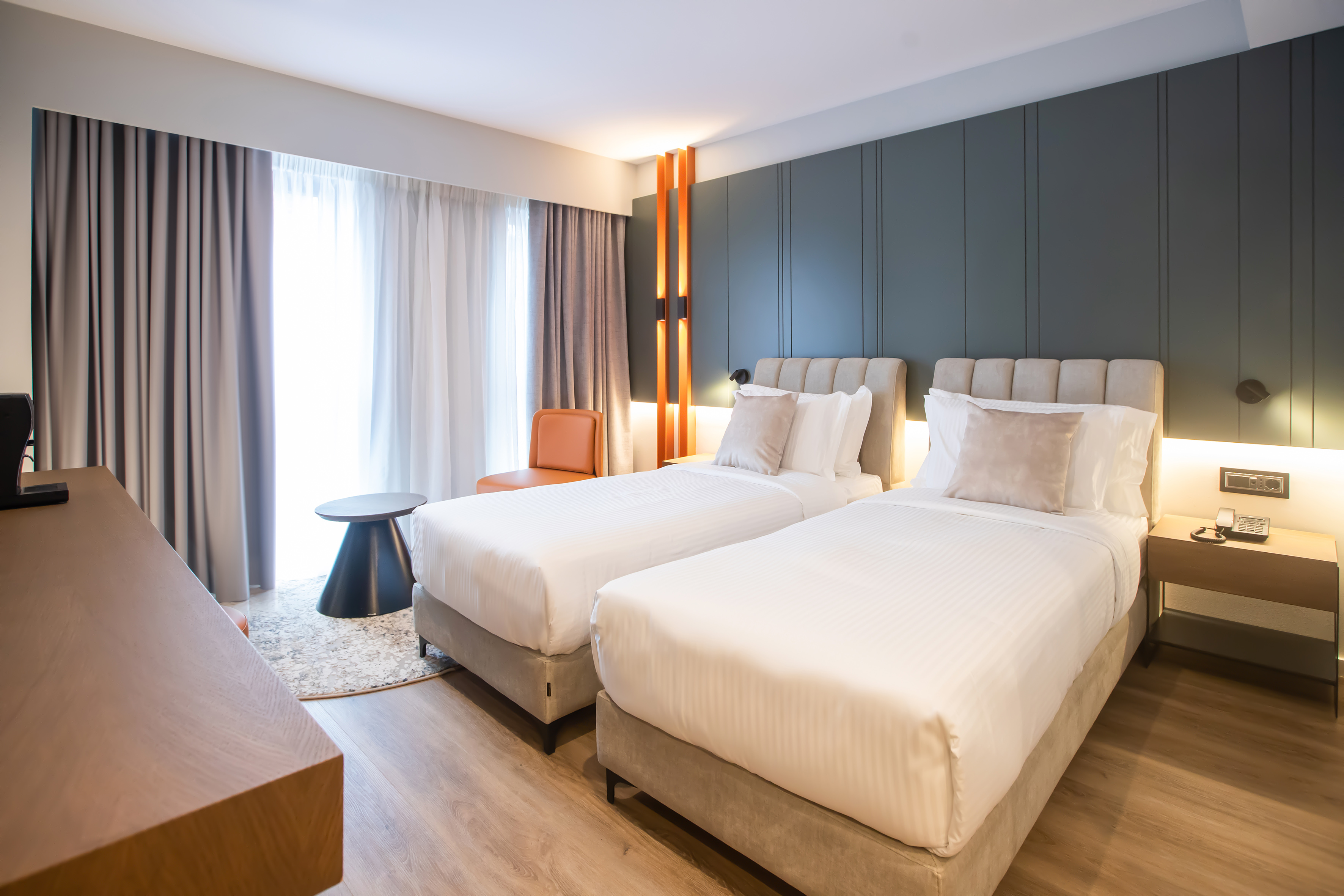 Modern hotel room with two twin beds, dark green accent wall, and wooden floor.