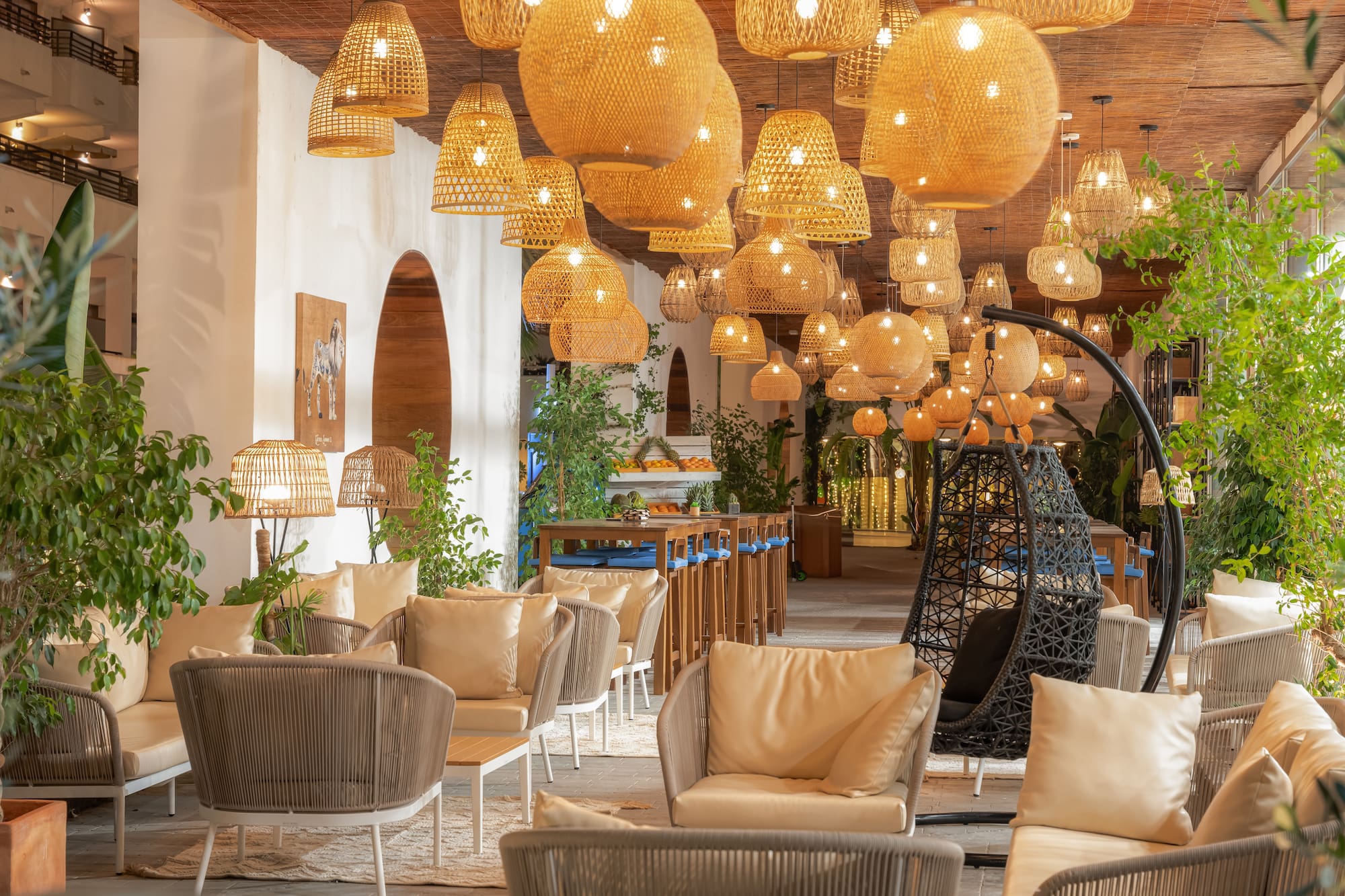 Acogedor lounge de restaurante con lámparas de mimbre y plantas naturales.
