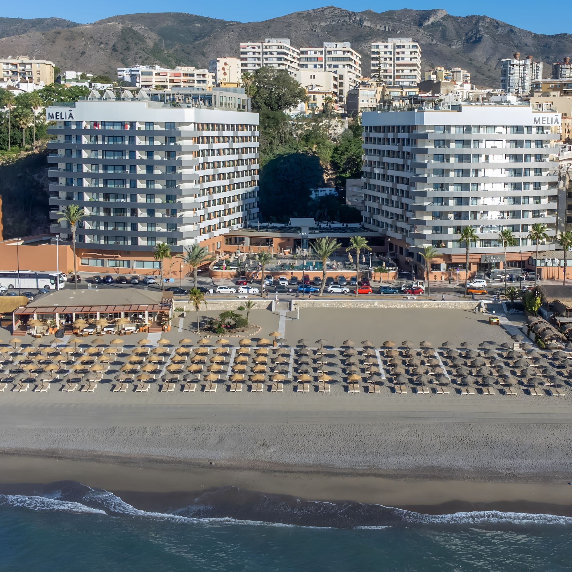 Meliá Marbella beach resort with sunbeds, palm trees, sea, and mountains.