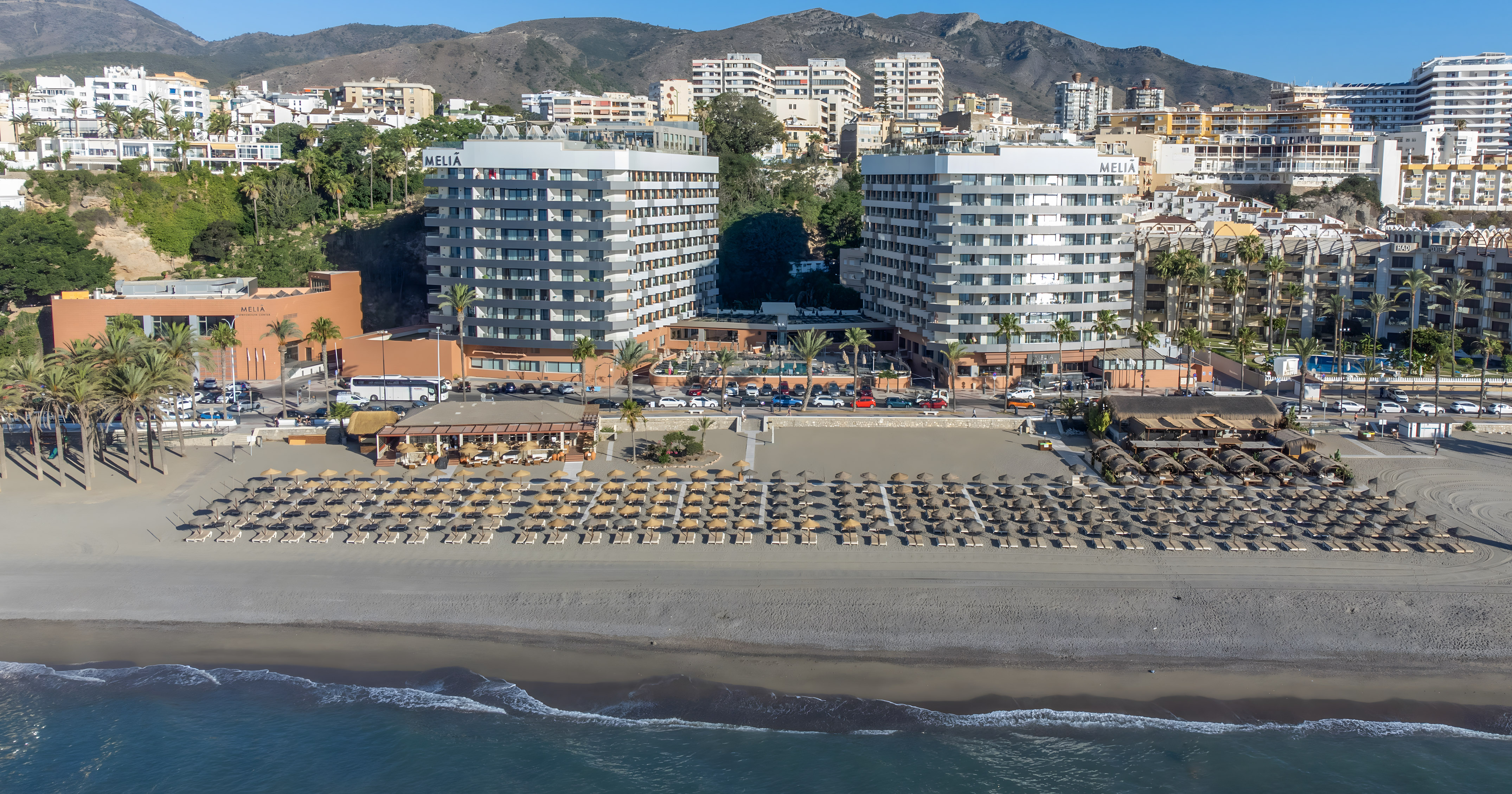Meliá Marbella beach resort with sunbeds, palm trees, sea, and mountains.