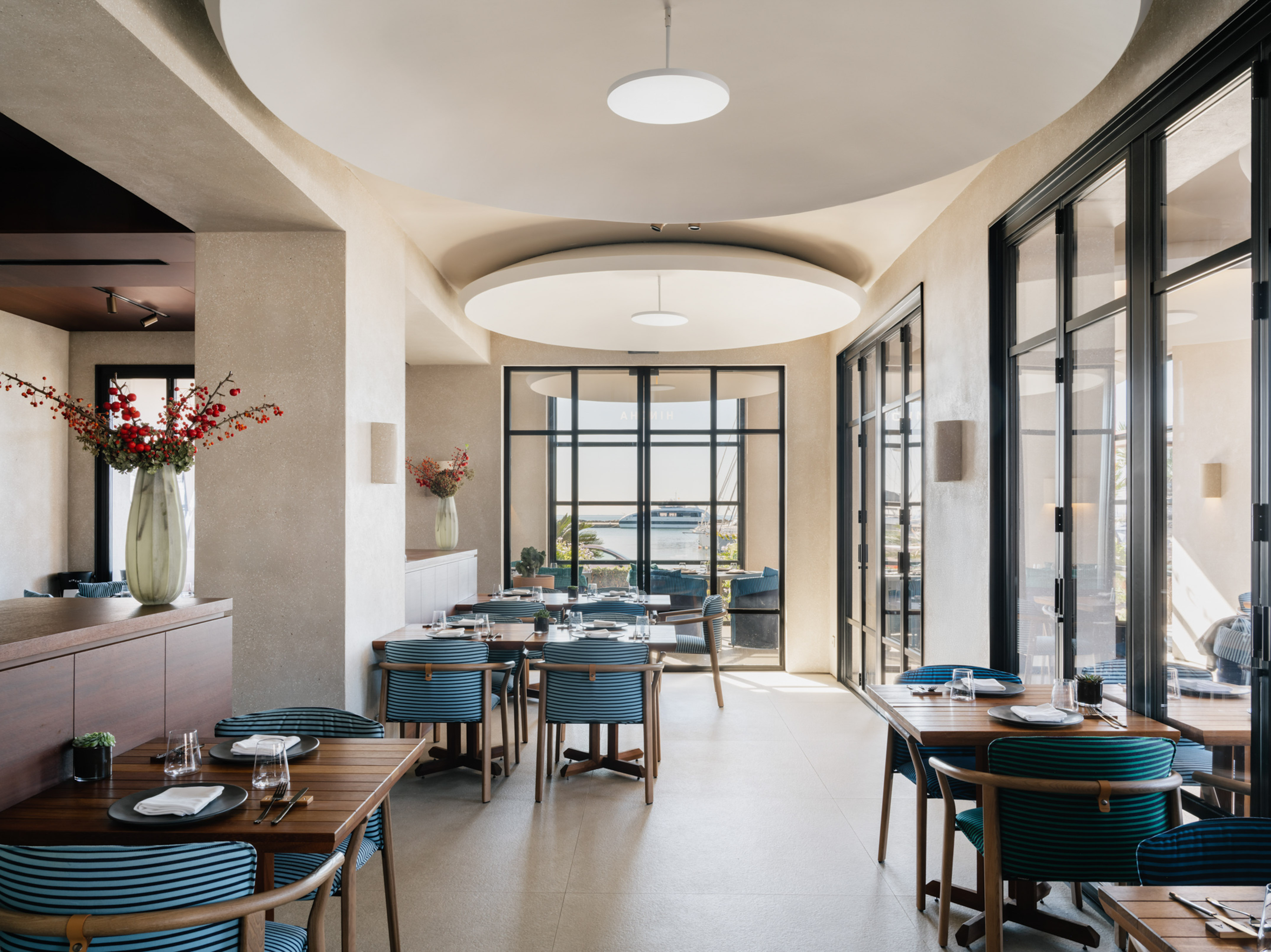 Modern waterfront restaurant with blue chairs, wooden tables, and harbor view.