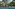 Tropical resort pool with lounge seating, sun umbrellas, and lush trees.