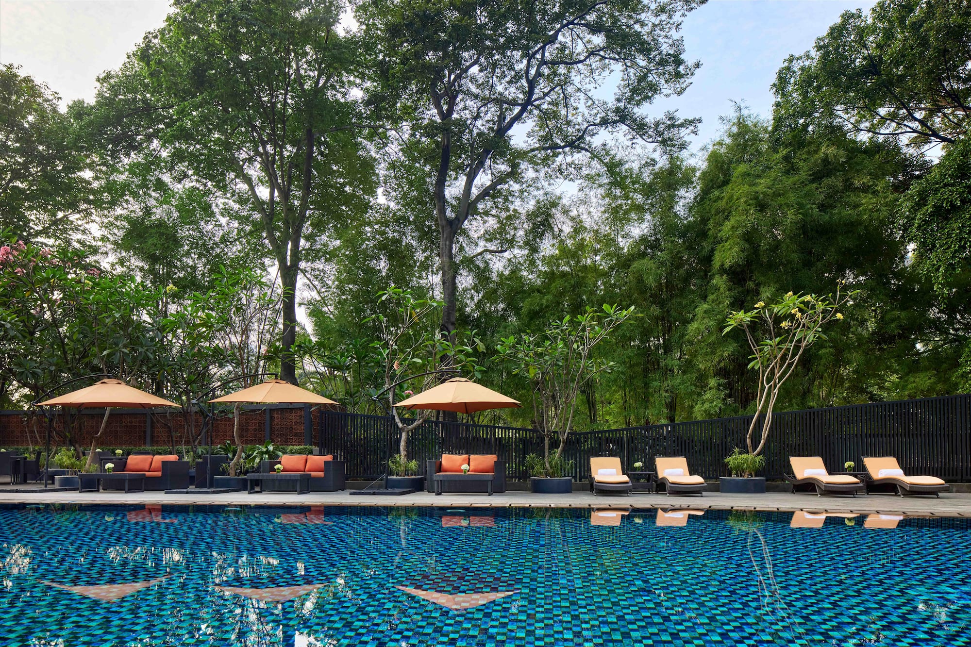 Tropical resort pool with lounge seating, sun umbrellas, and lush trees.