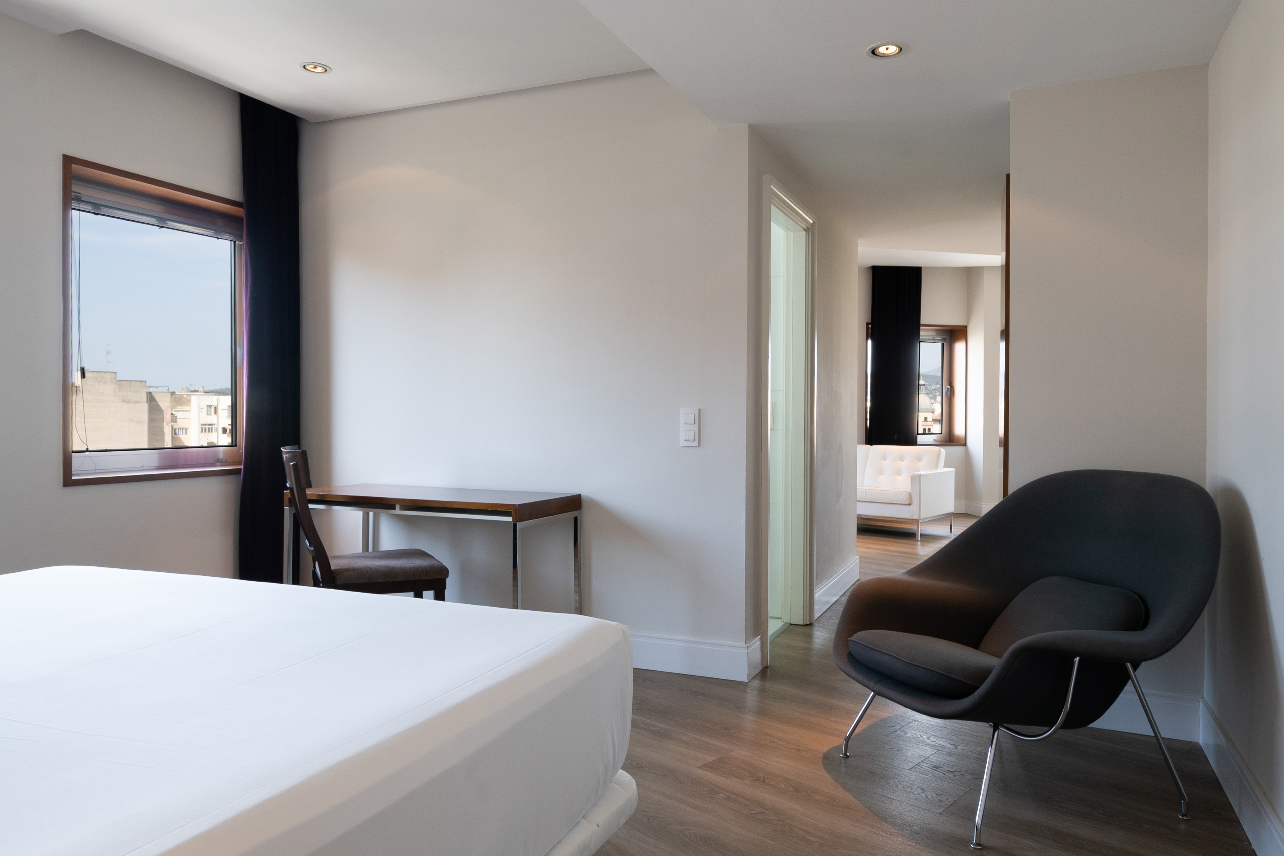 Modern hotel room with bed, desk, city view window, and lounge armchair.