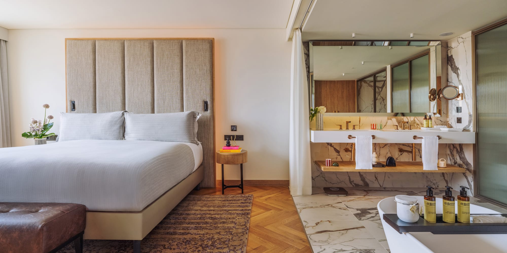 Luxury hotel room with king bed, tufted headboard, and open marble bathroom.