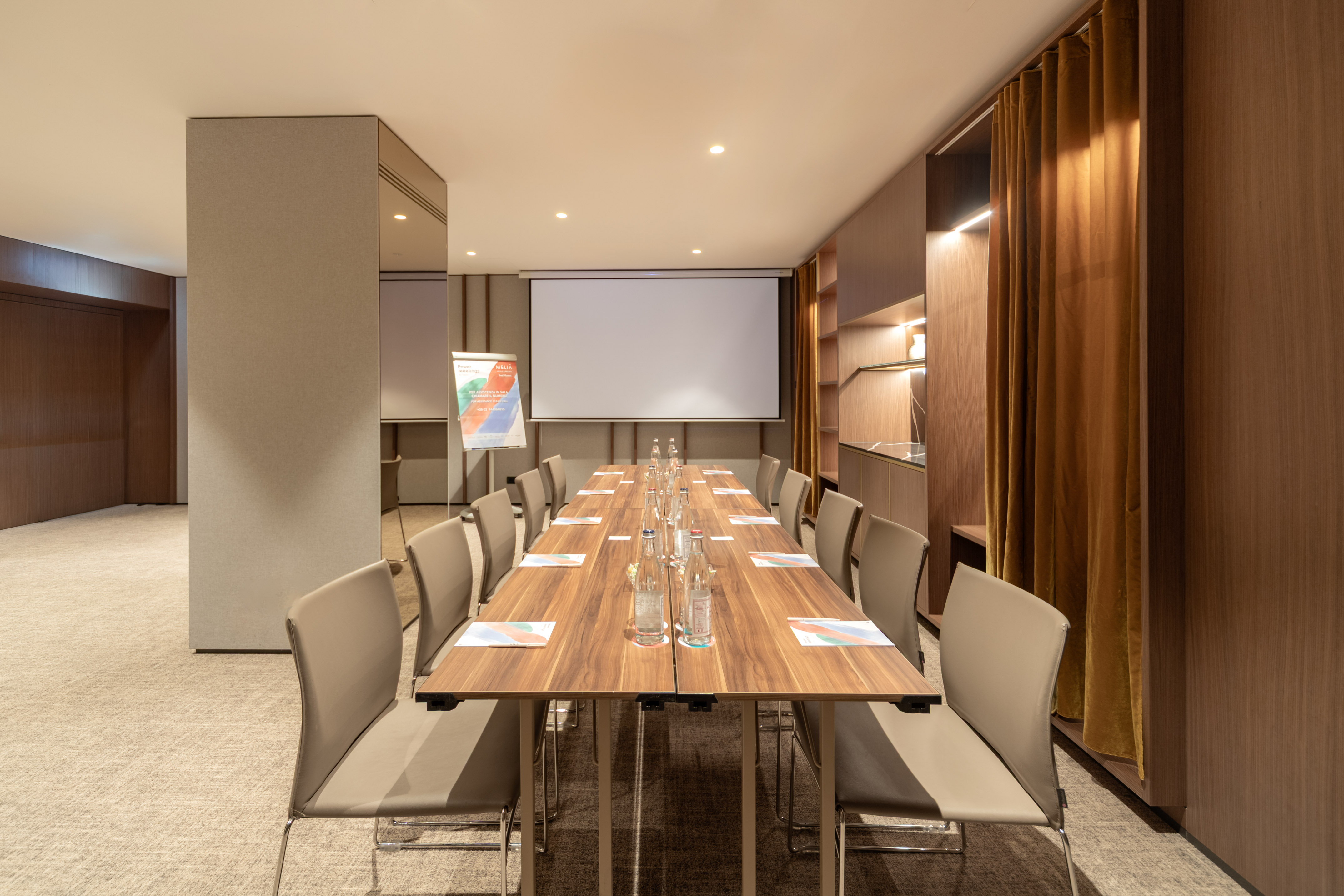 Hotel meeting room with long wooden table, chairs, and projector screen.