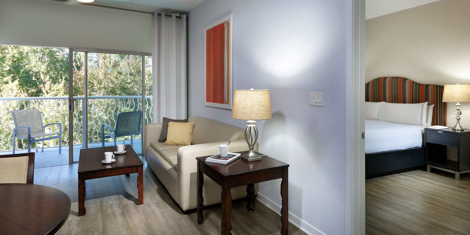 Modern hotel suite living room, balcony, sofa, and connected bedroom.