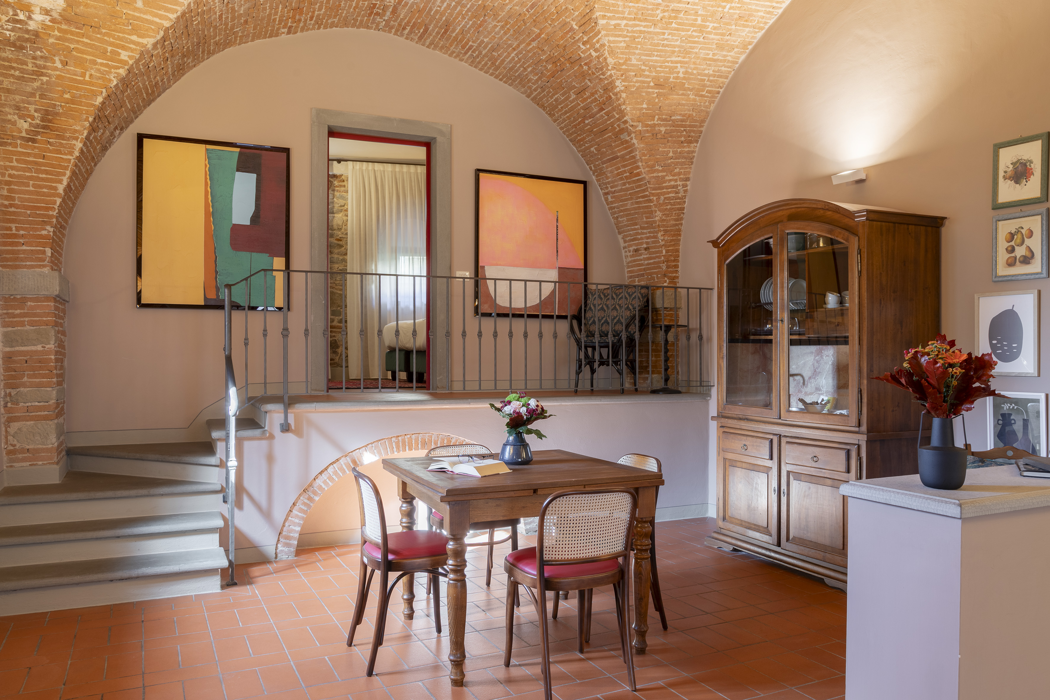 Italian villa dining: brick arches, terracotta floor, wooden table, and modern art.