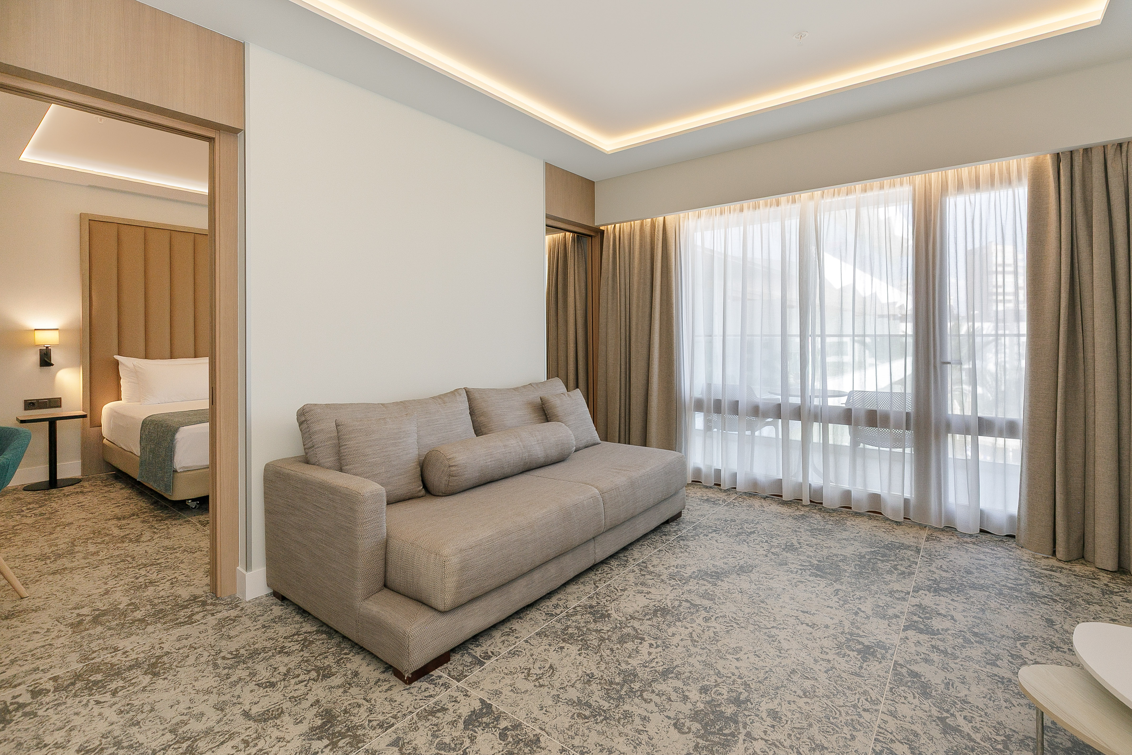 Modern hotel suite living room with sofa, large window, and open bedroom.