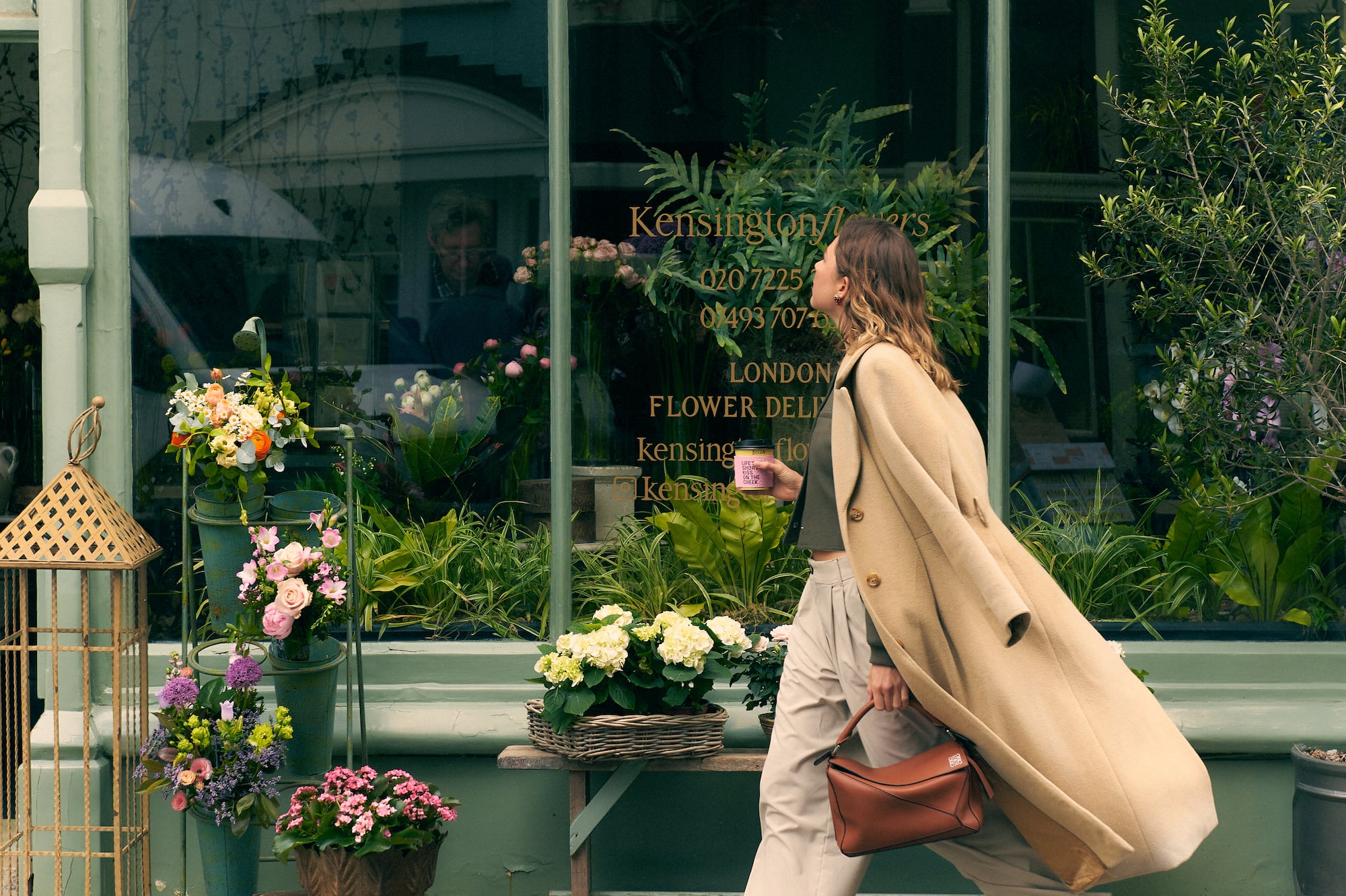 Mujer elegante pasa por la floristería Kensingtonflowers en Londres, con arreglos florales.