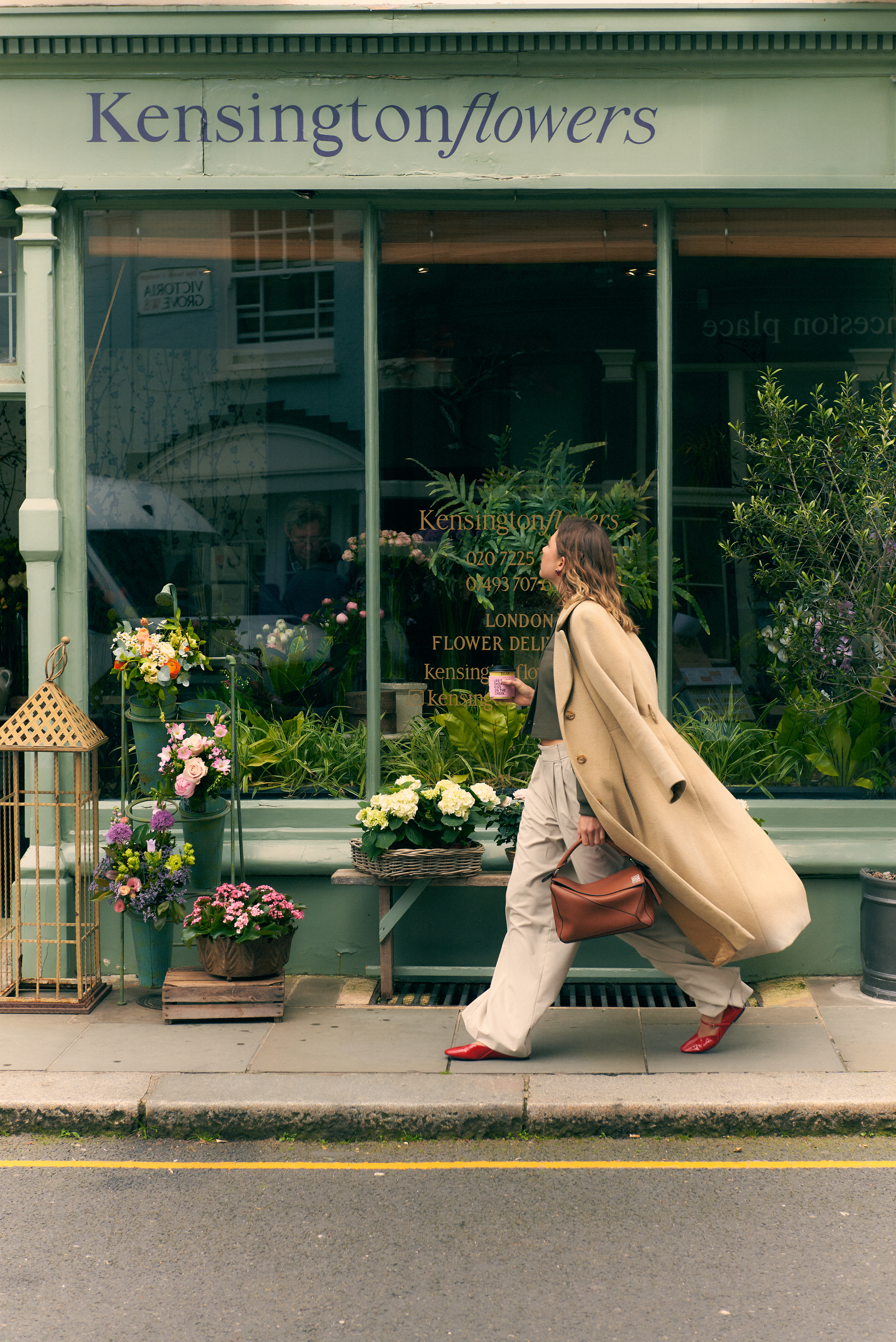 Mujer elegante pasa por la floristería Kensingtonflowers en Londres, con arreglos florales.