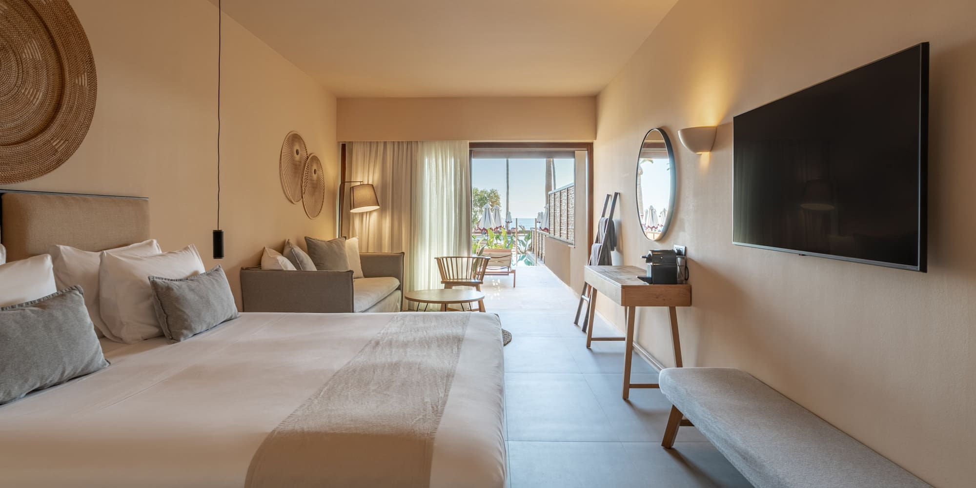 Hotel suite with modern bedroom, sofa, TV, and ocean view balcony.