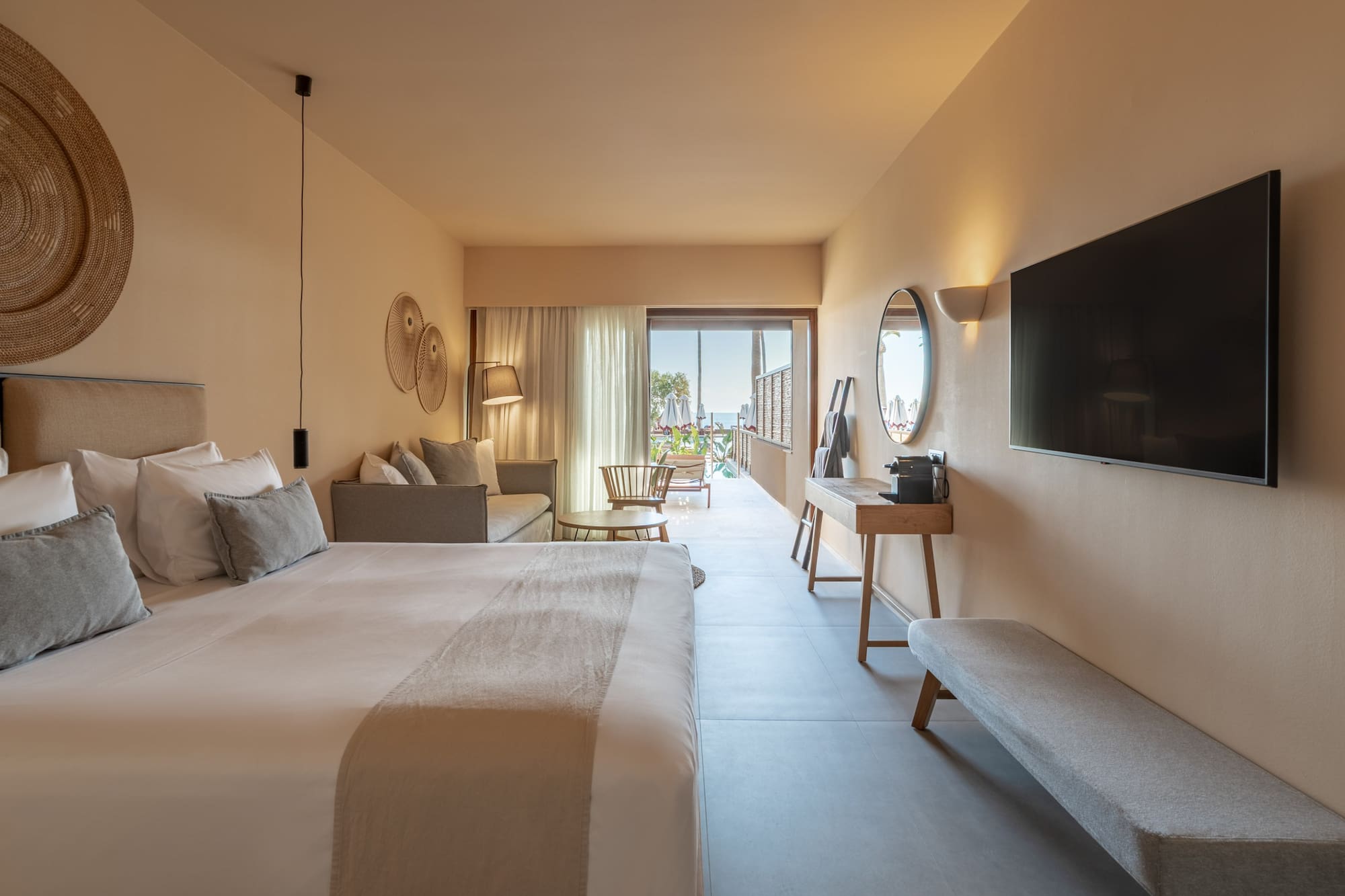 Hotel suite with modern bedroom, sofa, TV, and ocean view balcony.