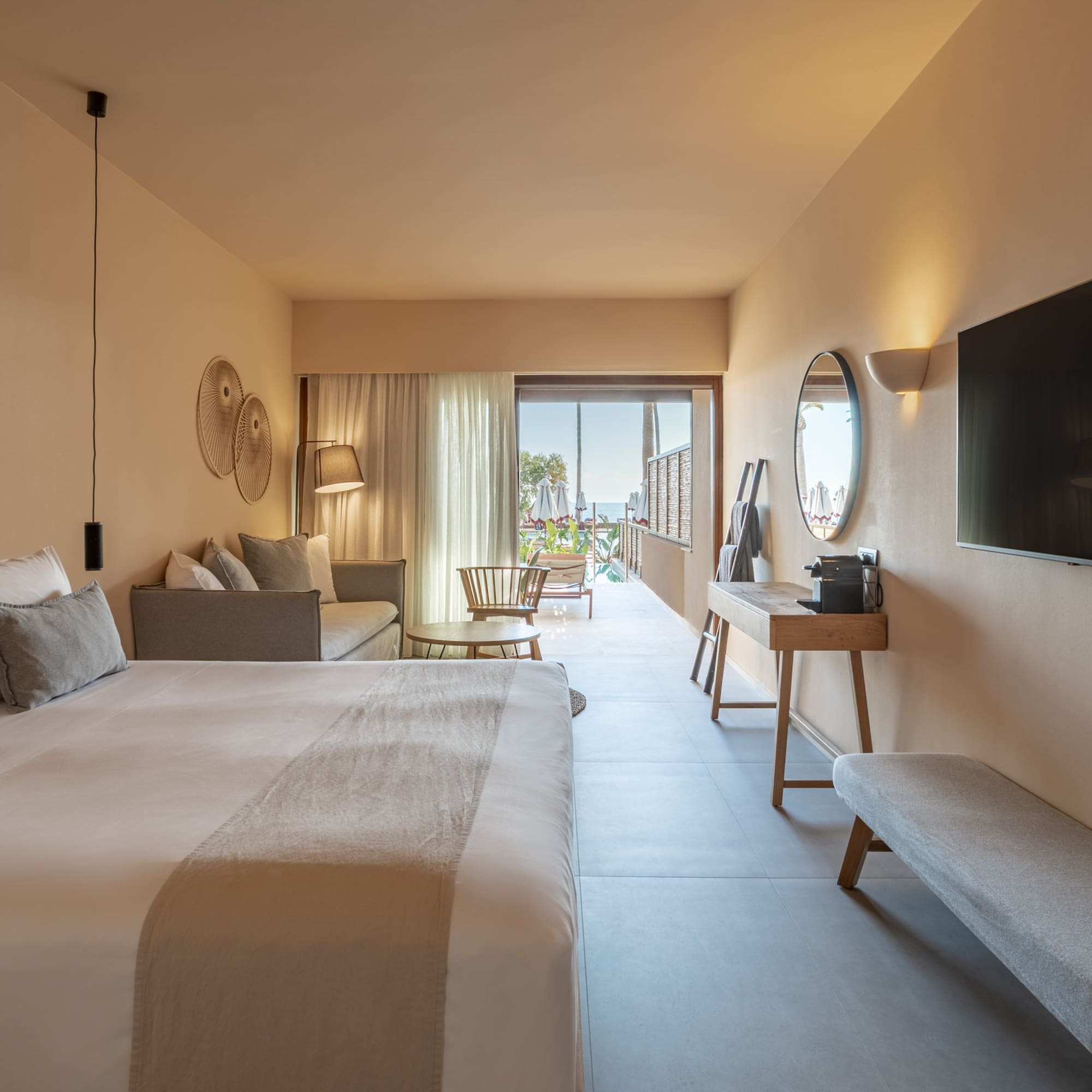Hotel suite with modern bedroom, sofa, TV, and ocean view balcony.