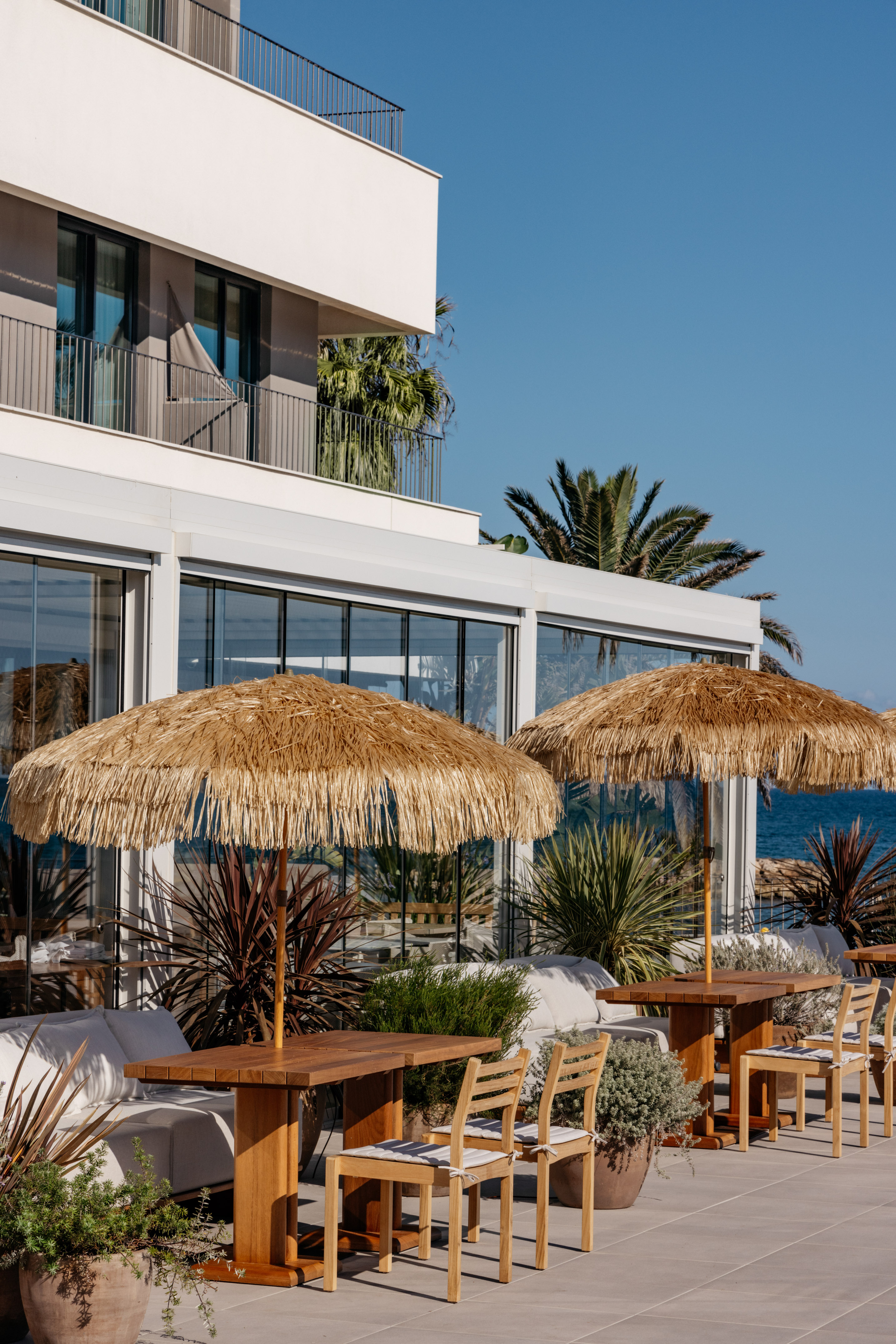 Beachfront dining patio with straw umbrellas, wooden tables, and modern hotel.