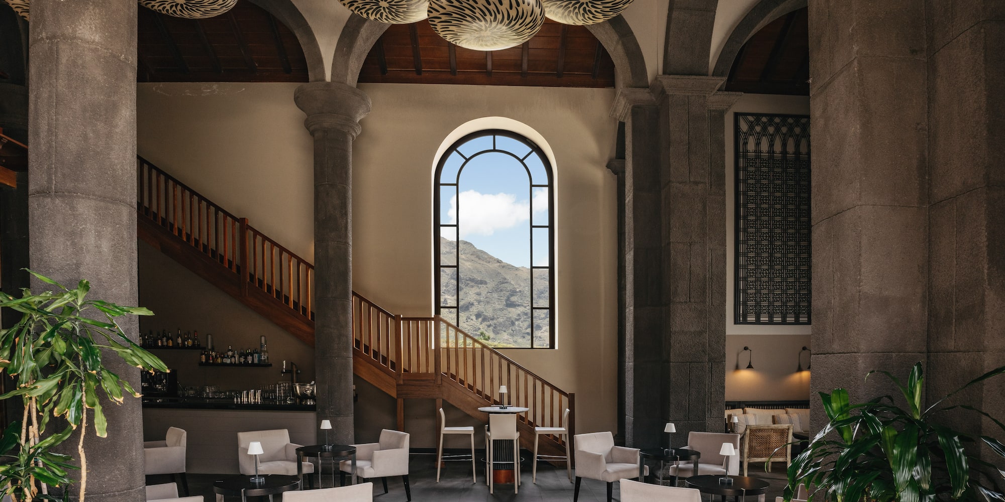 Hotel lobby with mountain view, stone pillars, arched window, and lounge seating.