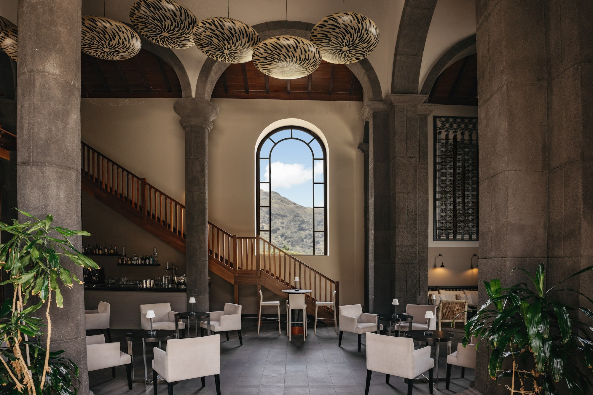 Elegant hotel lounge with stone arches, mountain view window, bar, and seating.