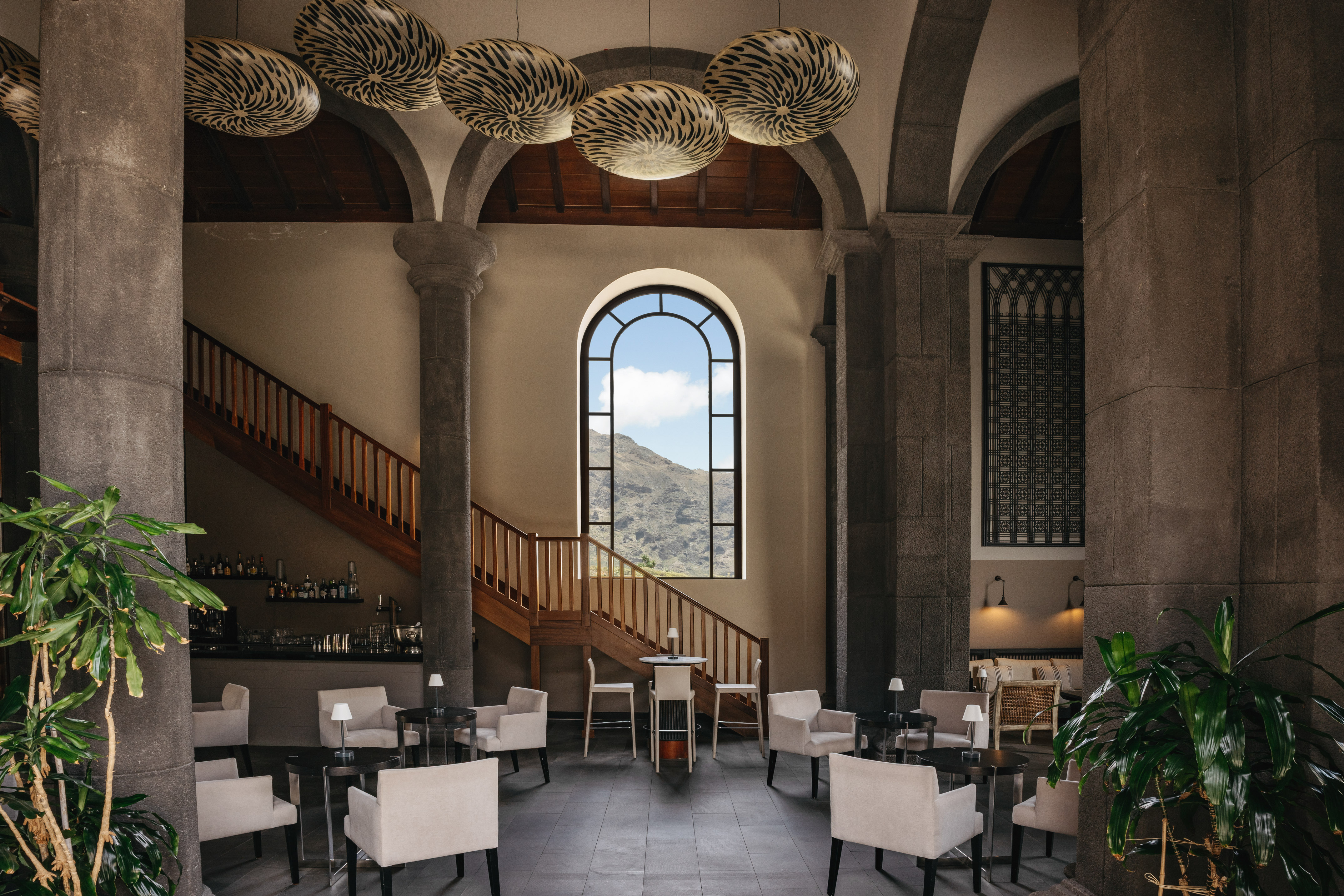 Elegant hotel lounge with stone arches, mountain view window, bar, and seating.