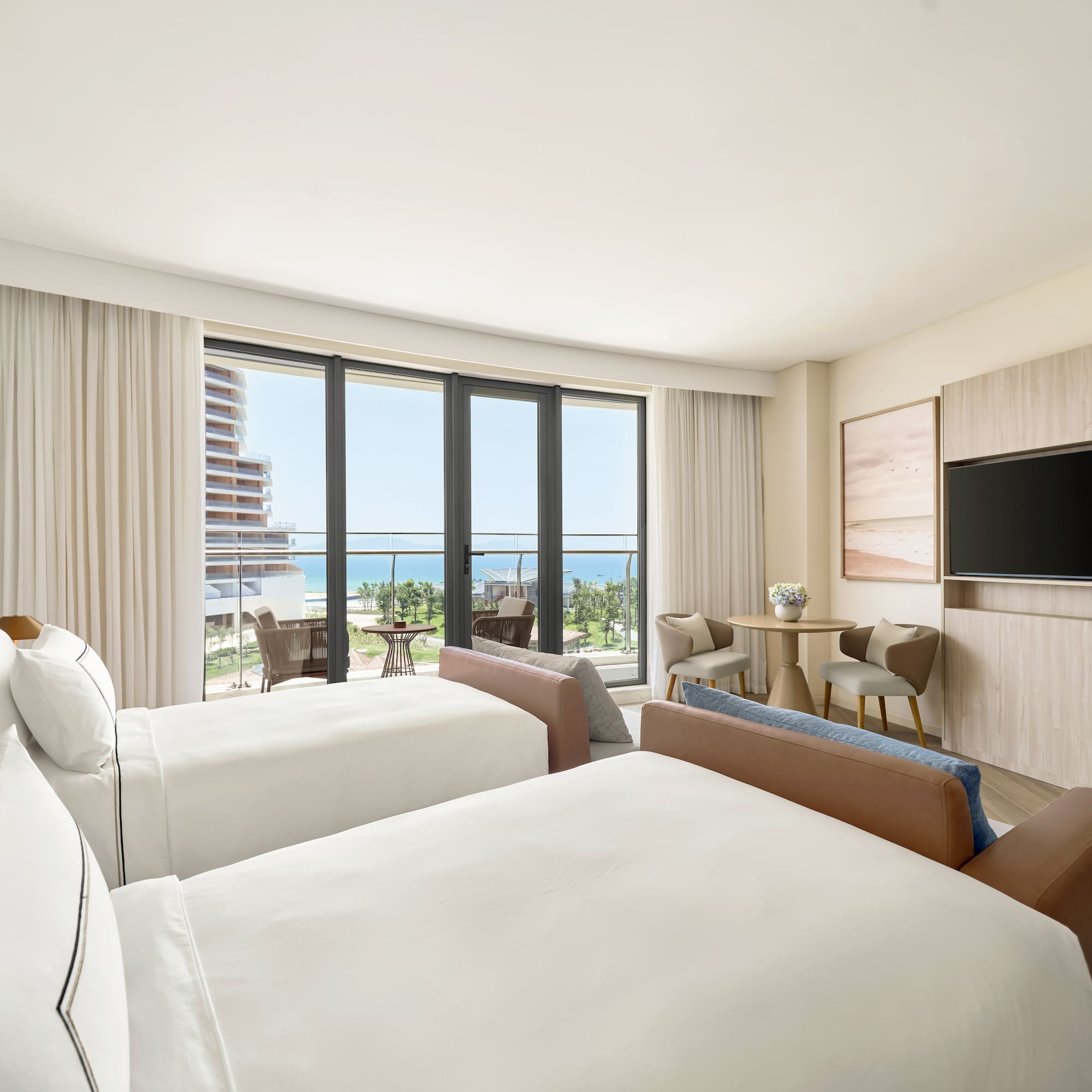 Hotel room with twin beds, ocean view balcony, and modern coastal design.