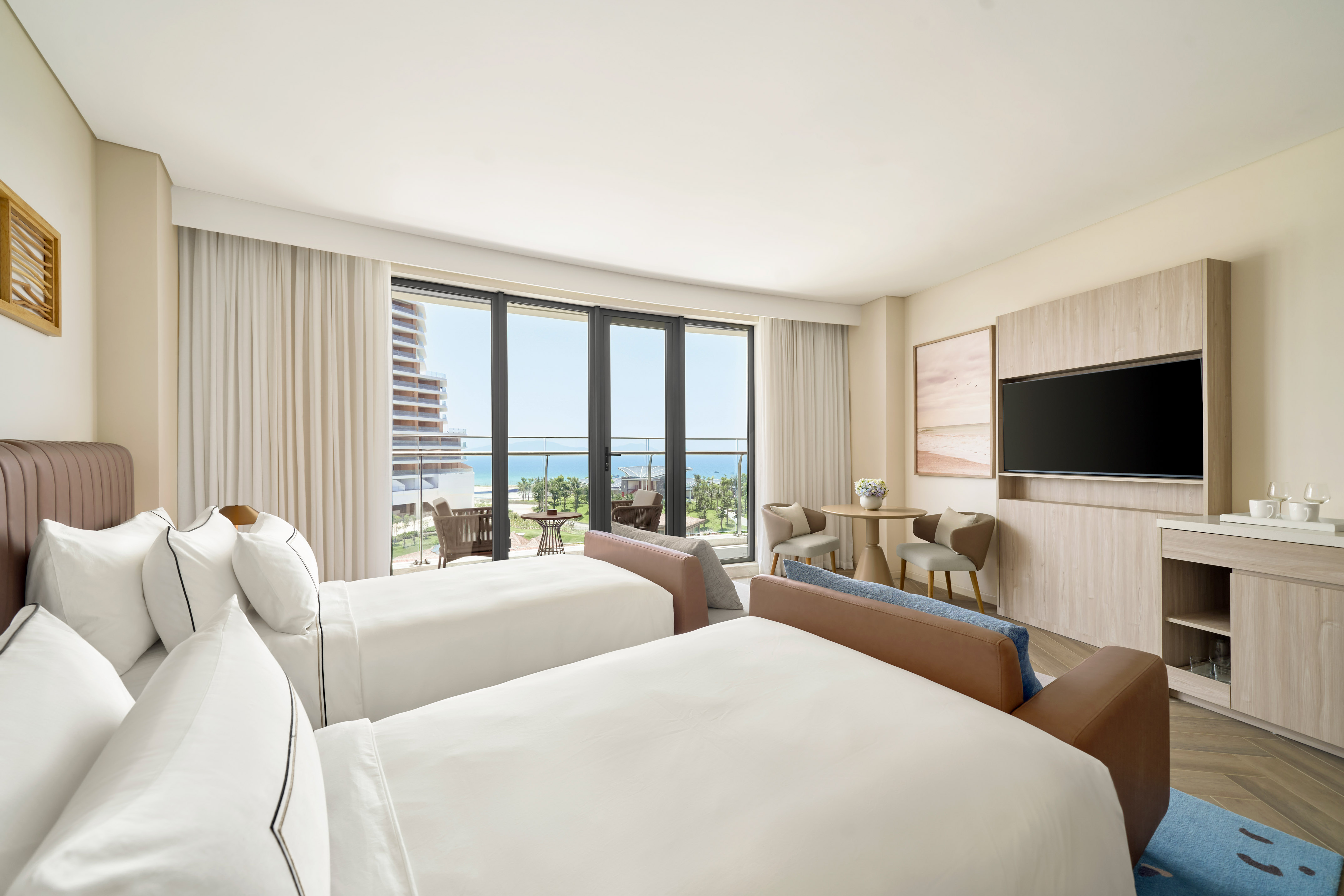 Hotel room with twin beds, ocean view balcony, and modern coastal design.