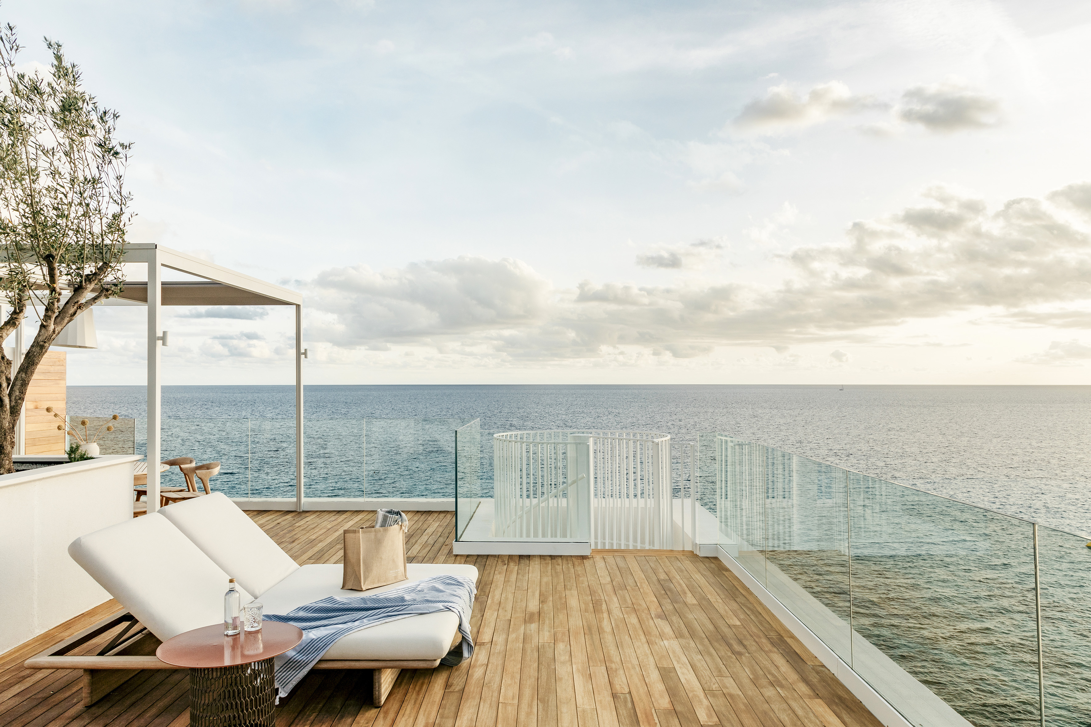Luxury hotel terrace with ocean view, lounge chairs, and wooden deck.