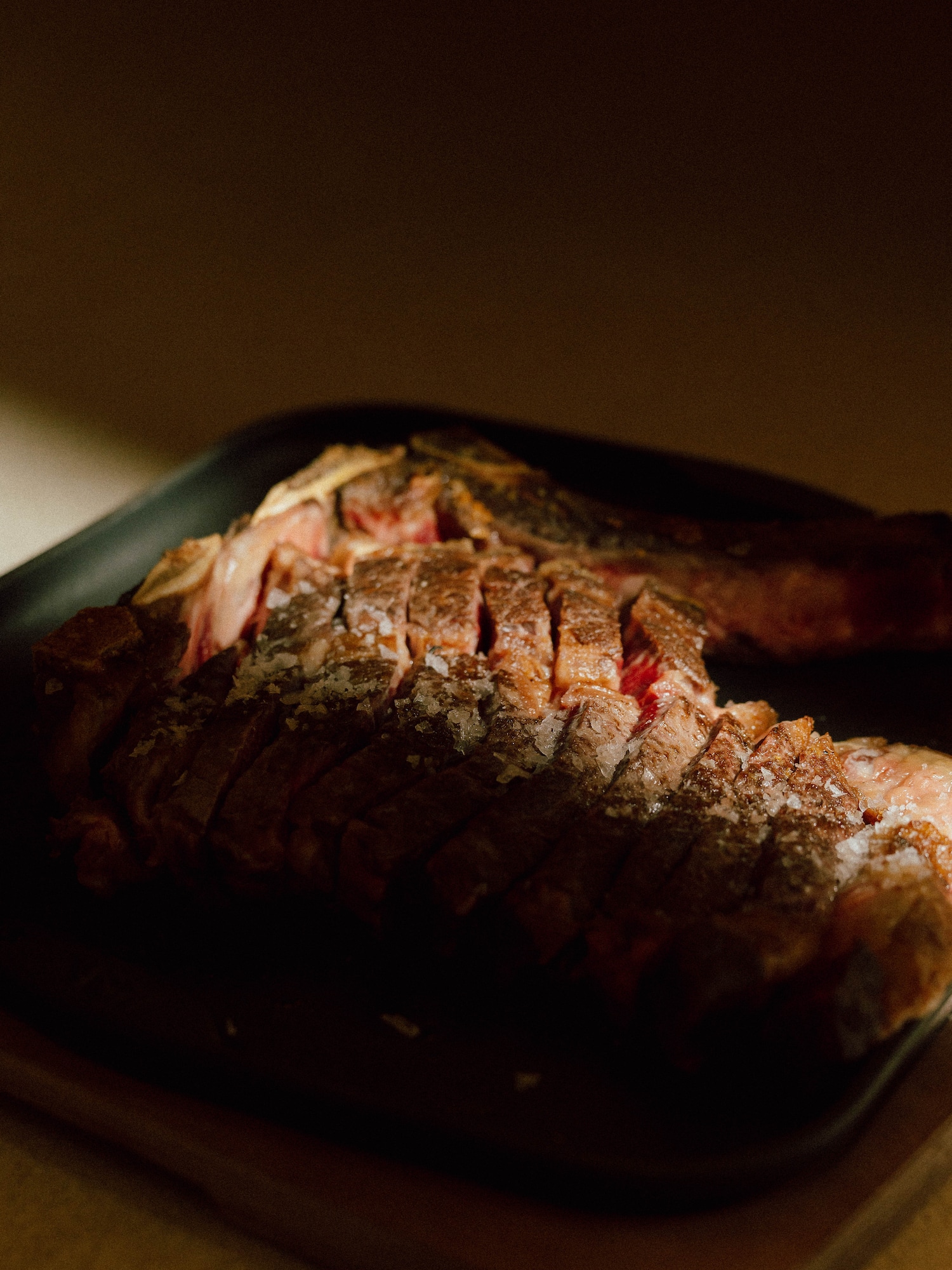 Sliced steak with coarse salt crystals on a dark serving platter.