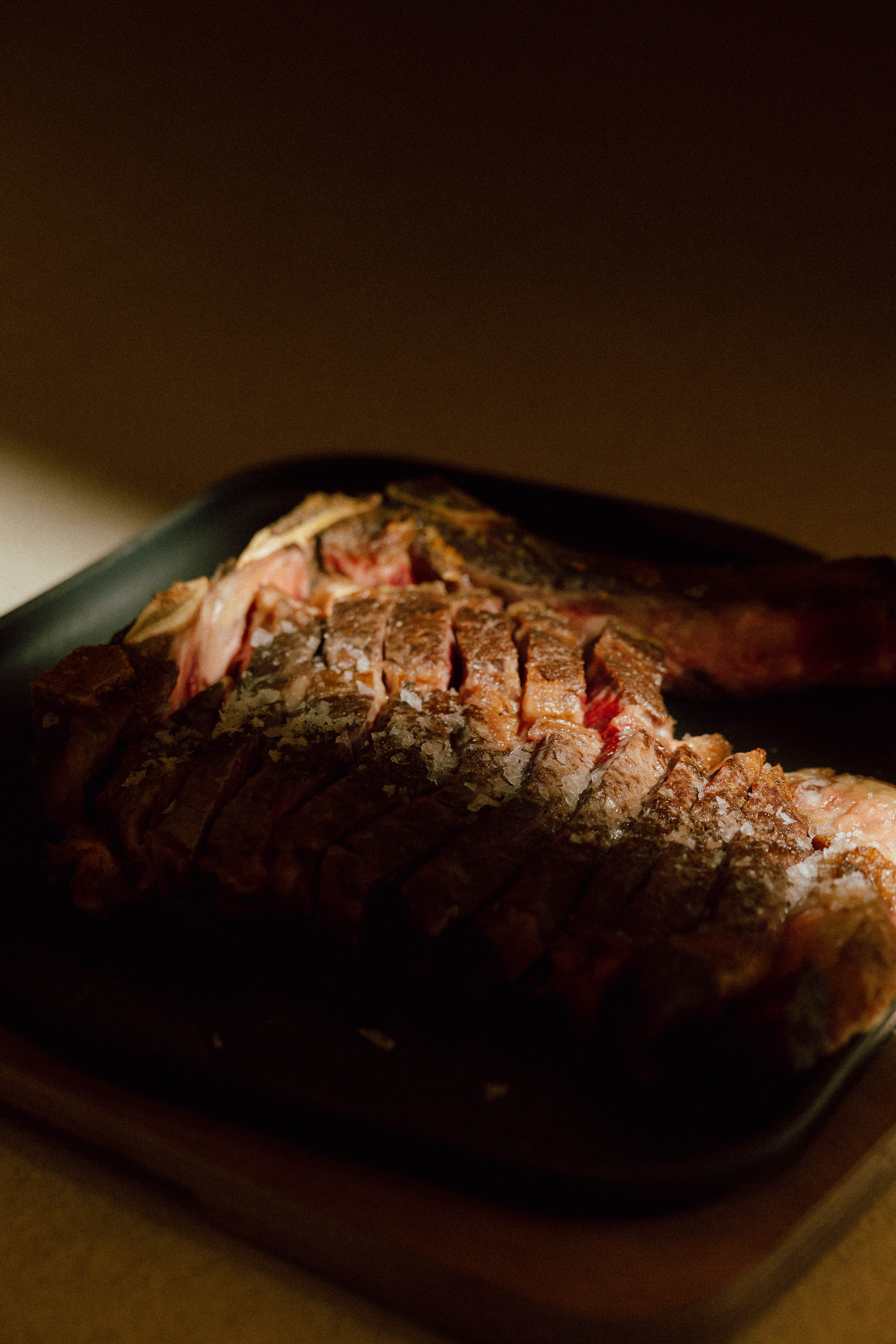 Sliced steak with coarse salt crystals on a dark serving platter.