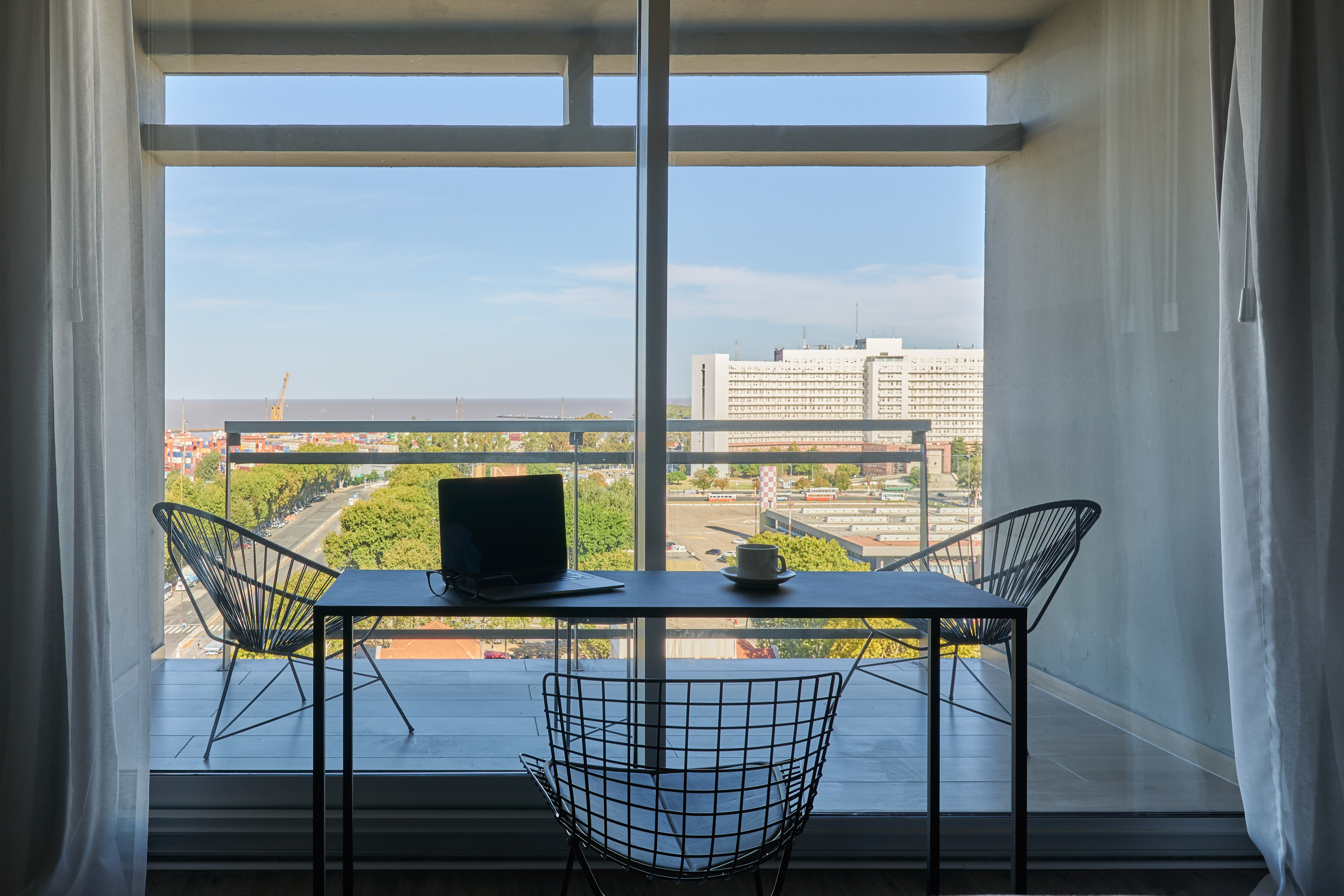Balcony home office with laptop, coffee, and urban water view.