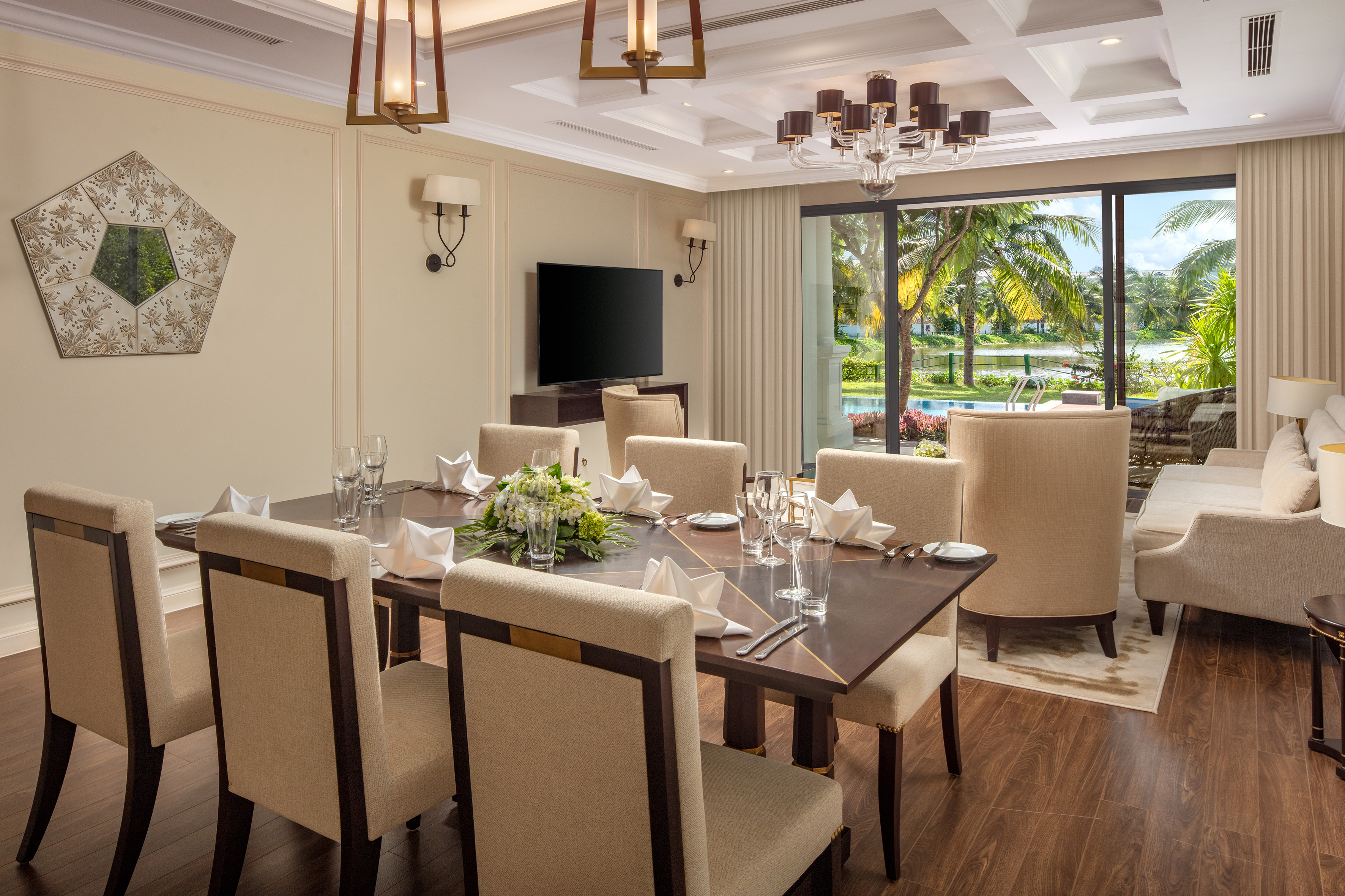 Luxurious dining room with set table, beige chairs, and scenic tropical pool view.