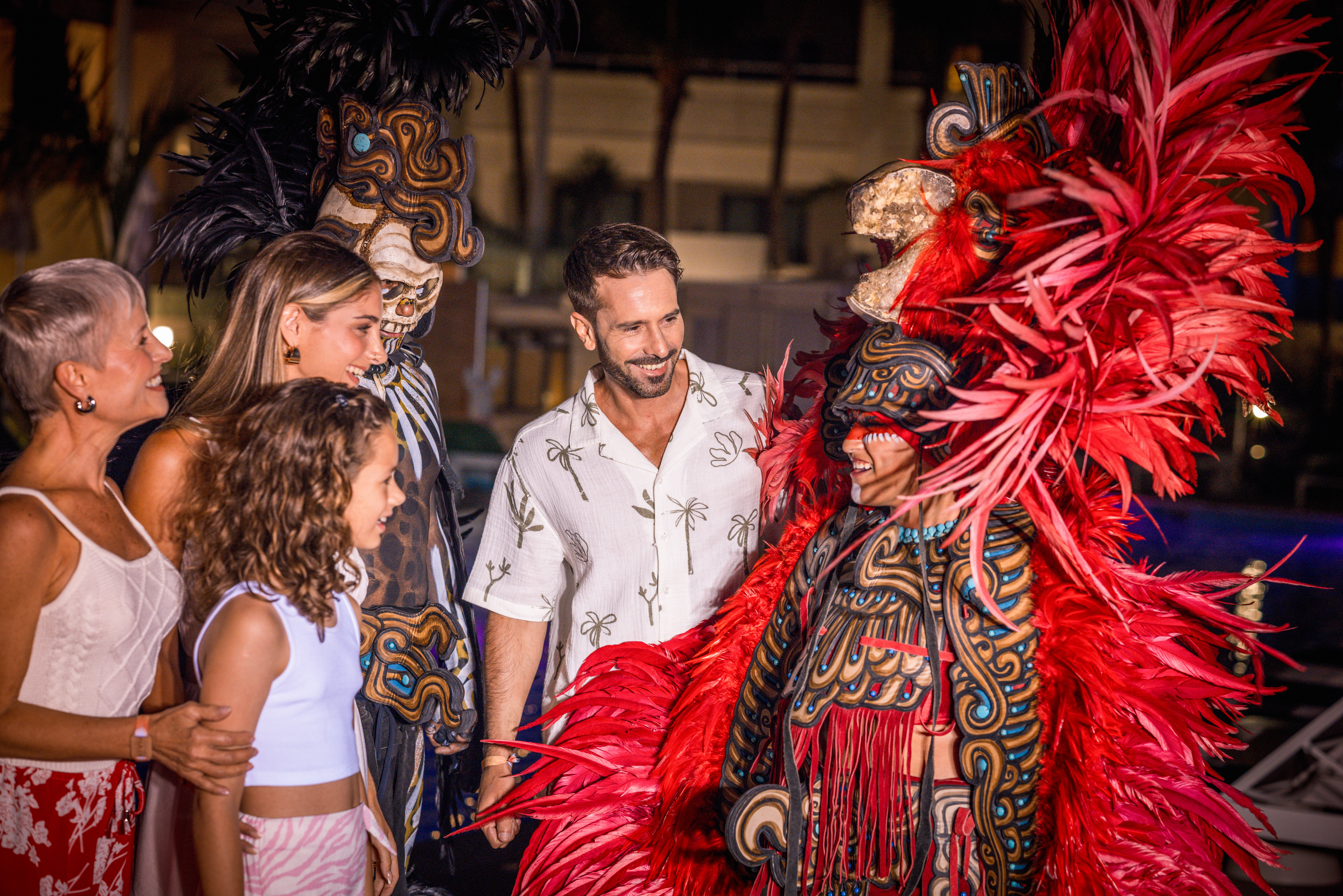 Guests smiling with performers in elaborate feathered costumes and masks.