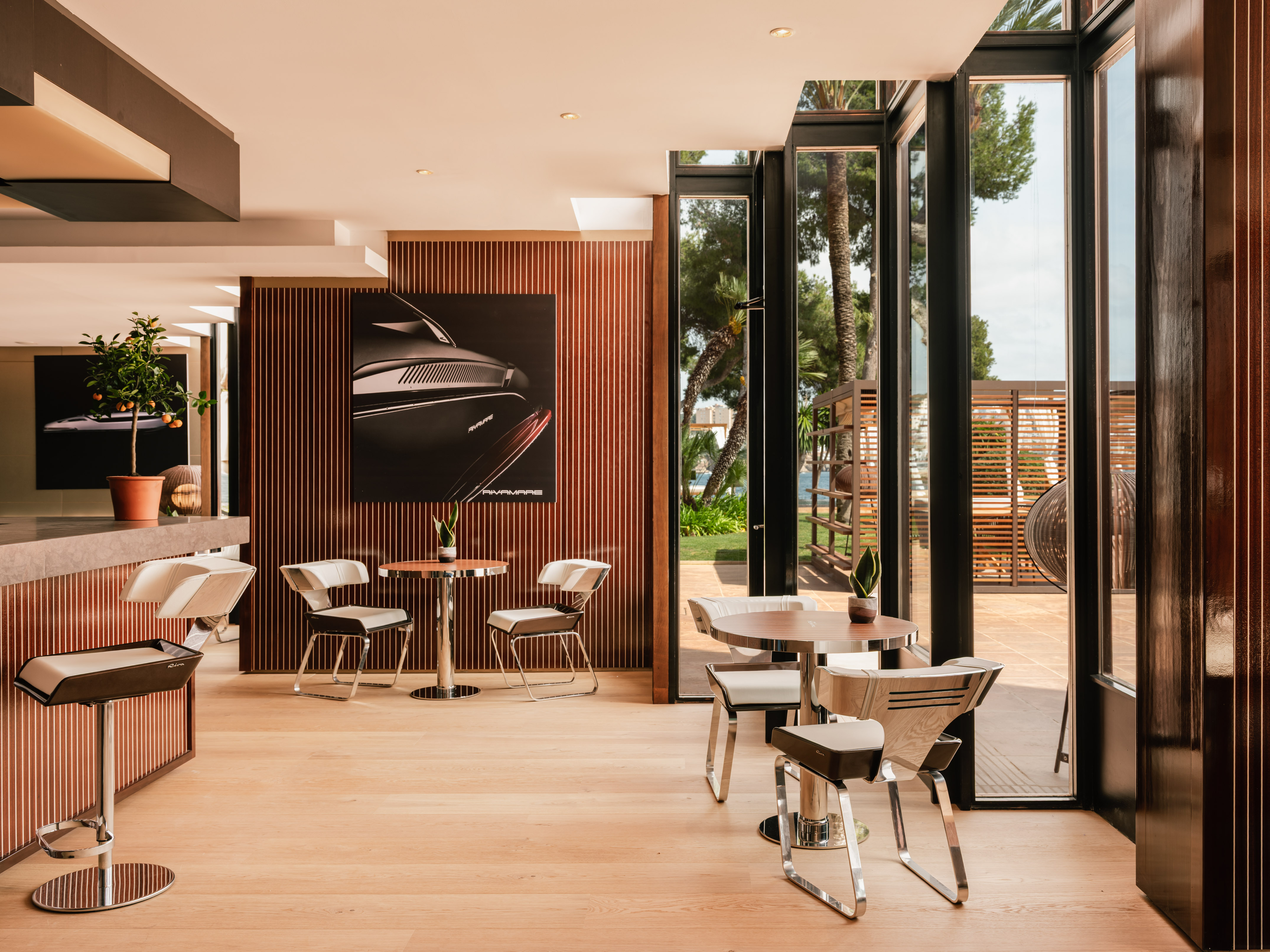 Modern lounge with RivaMares yacht art, sleek furniture, and outdoor garden view.