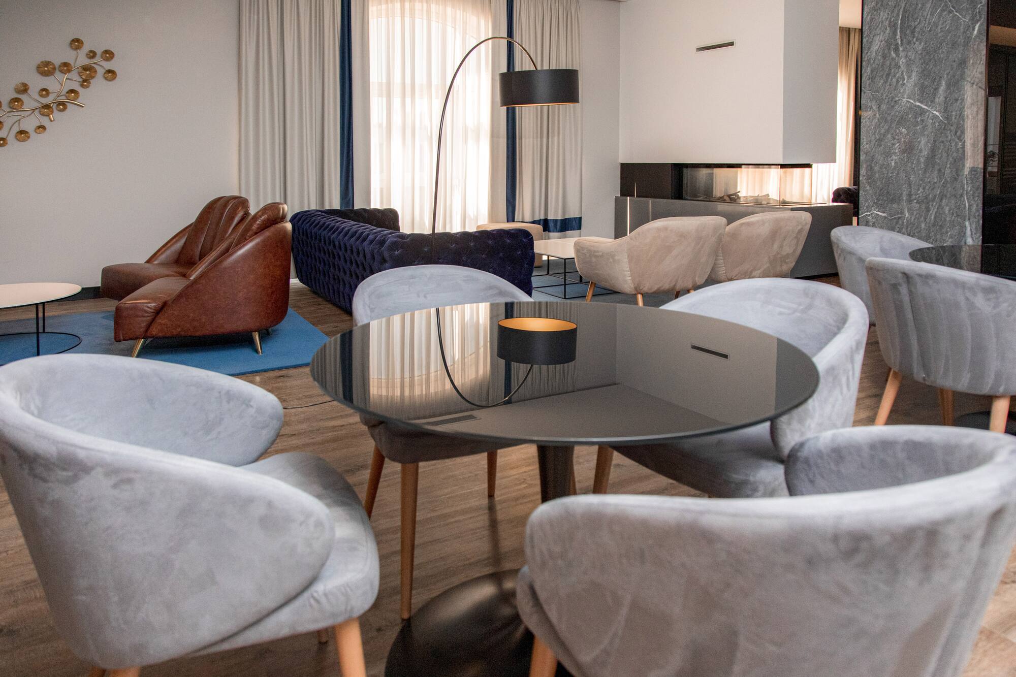 Modern lounge with grey velvet chairs, brown leather armchairs, and blue sofa.