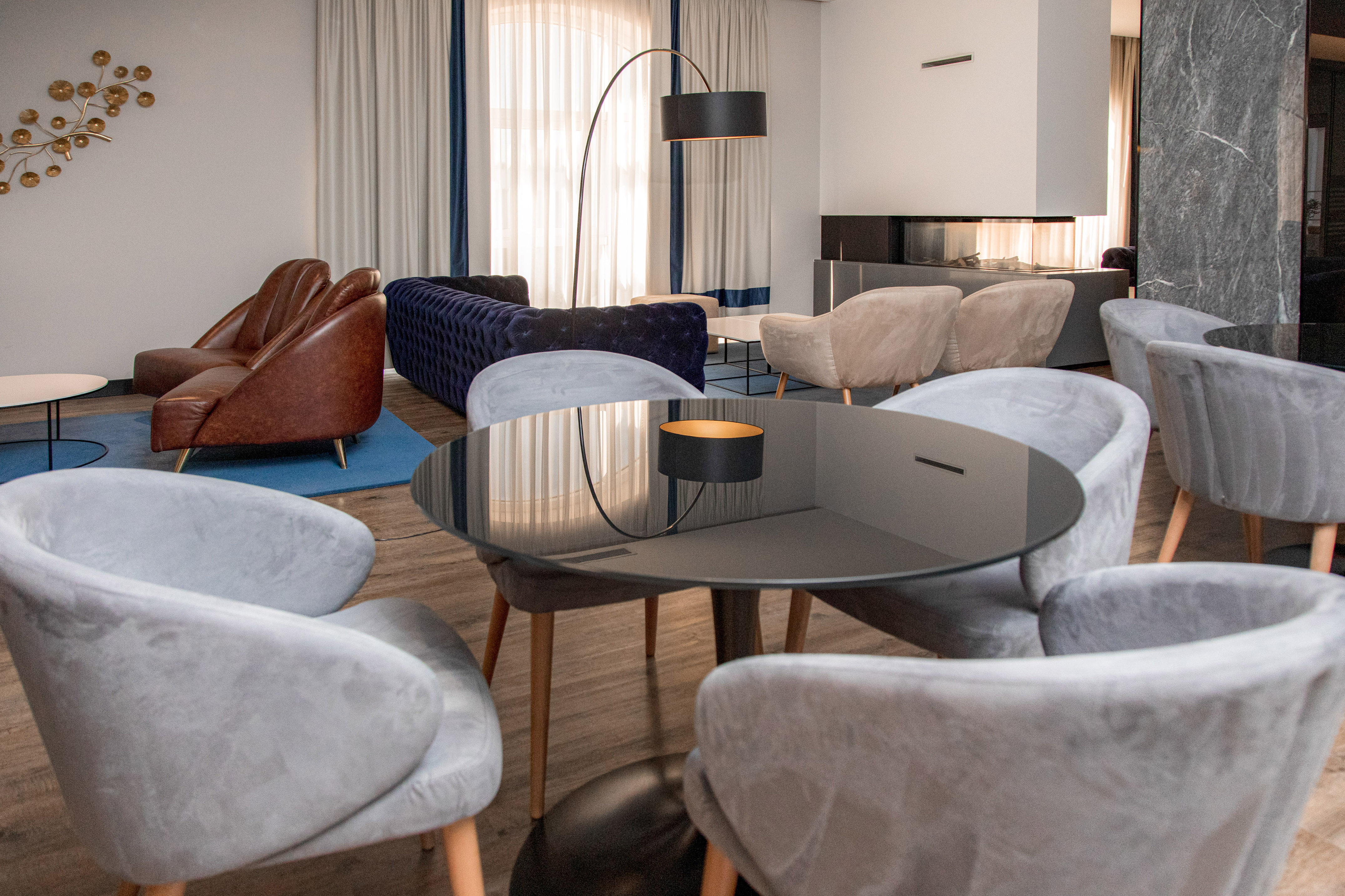 Modern lounge with grey velvet chairs, brown leather armchairs, and blue sofa.