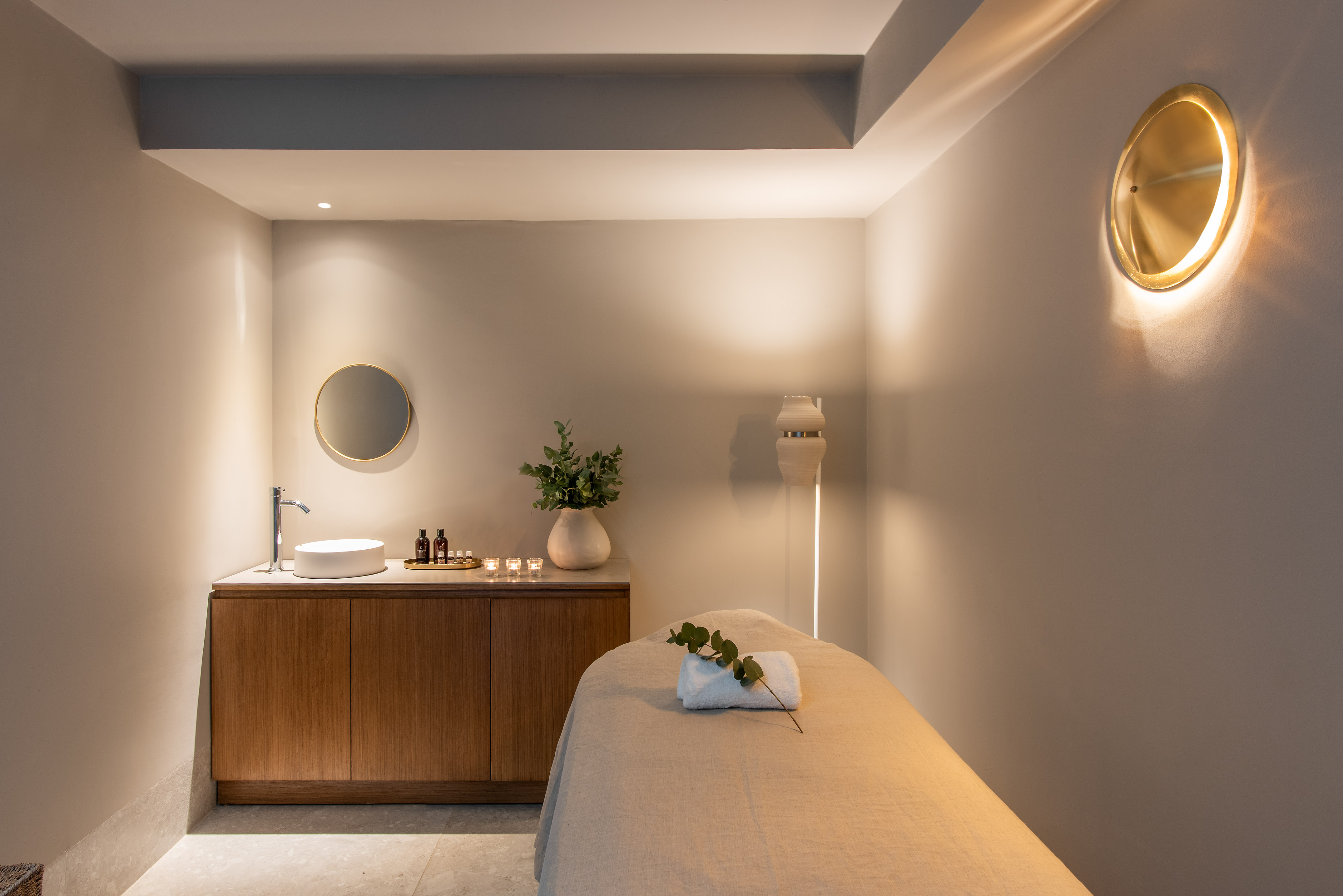 Serene spa massage treatment room with modern vanity, warm lighting, and eucalyptus.