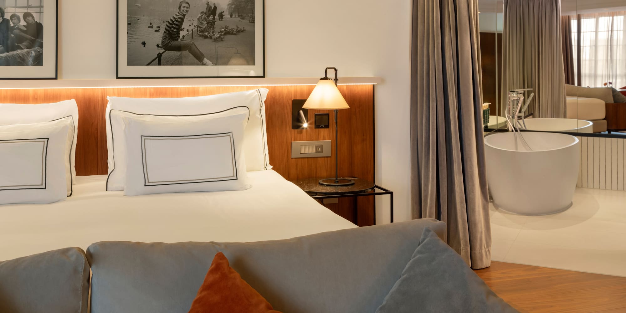 Modern hotel room with king bed, sofa, and freestanding bathtub.