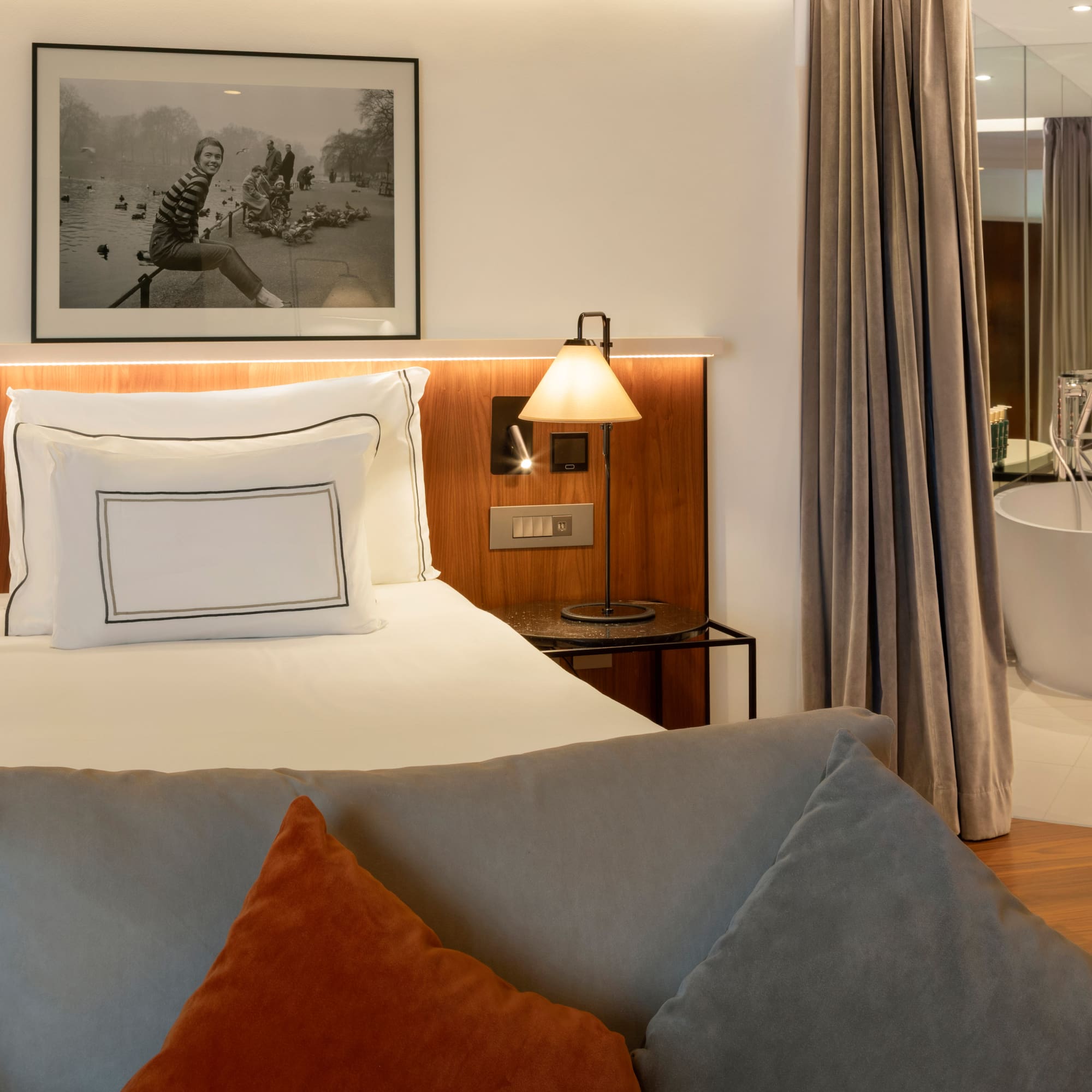 Modern hotel room with king bed, sofa, and freestanding bathtub.