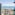 Beachfront hotel view with ocean, sandy beach, palm trees, and building balconies.
