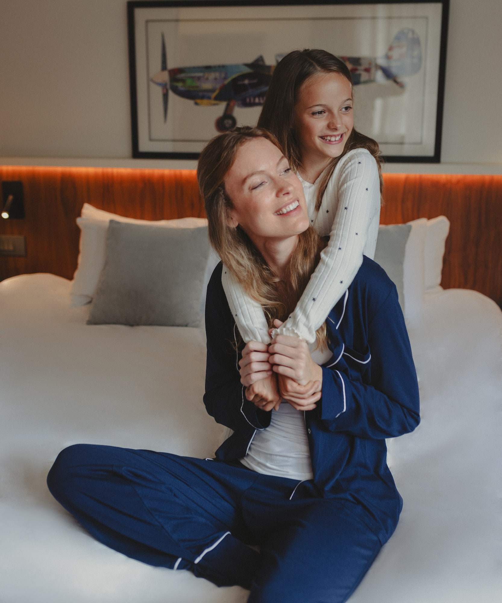 Smiling mother and daughter in pajamas hugging on a bed.