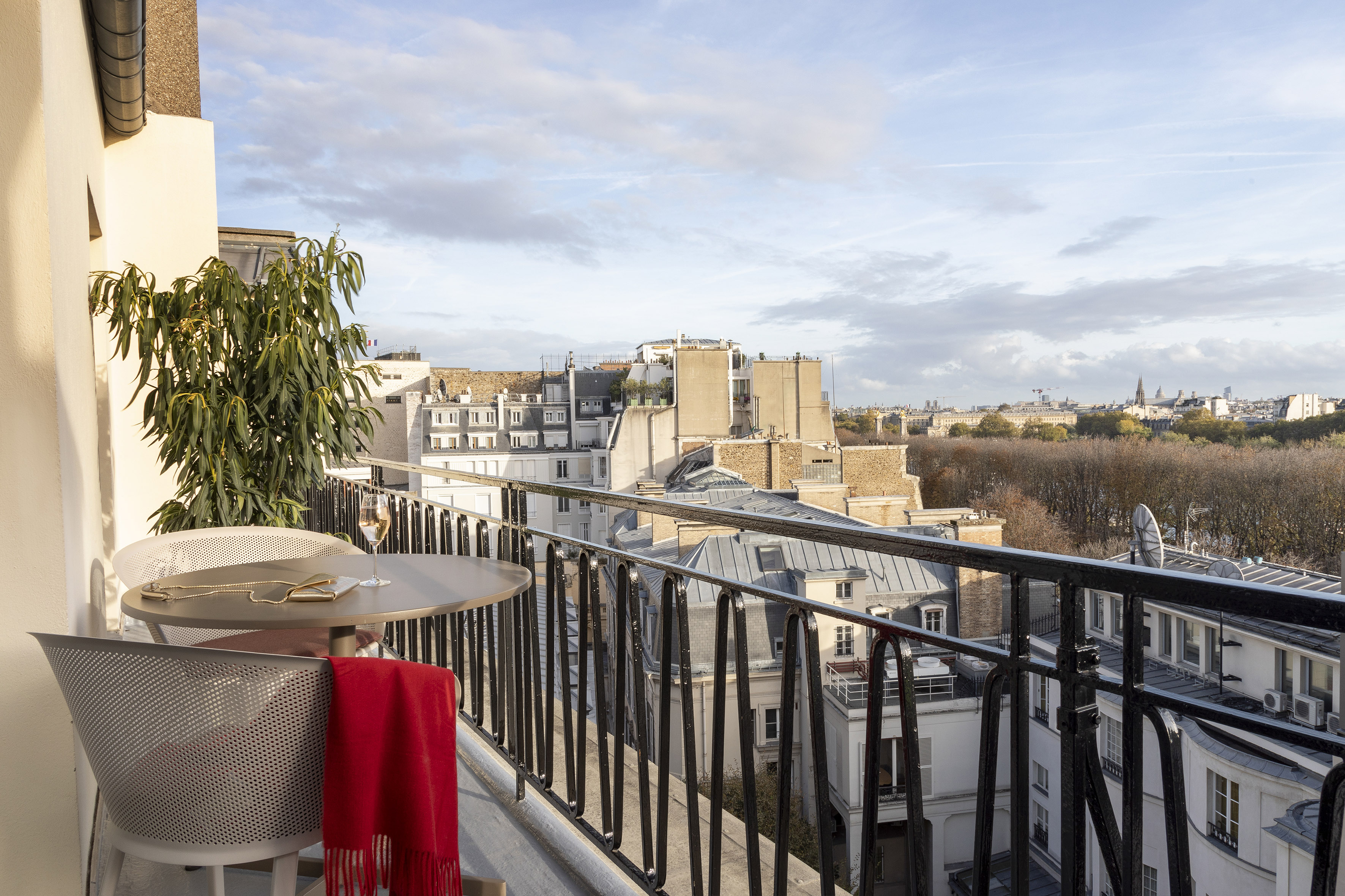 Parisian apartment balcony with table, chairs, wine, and city view.