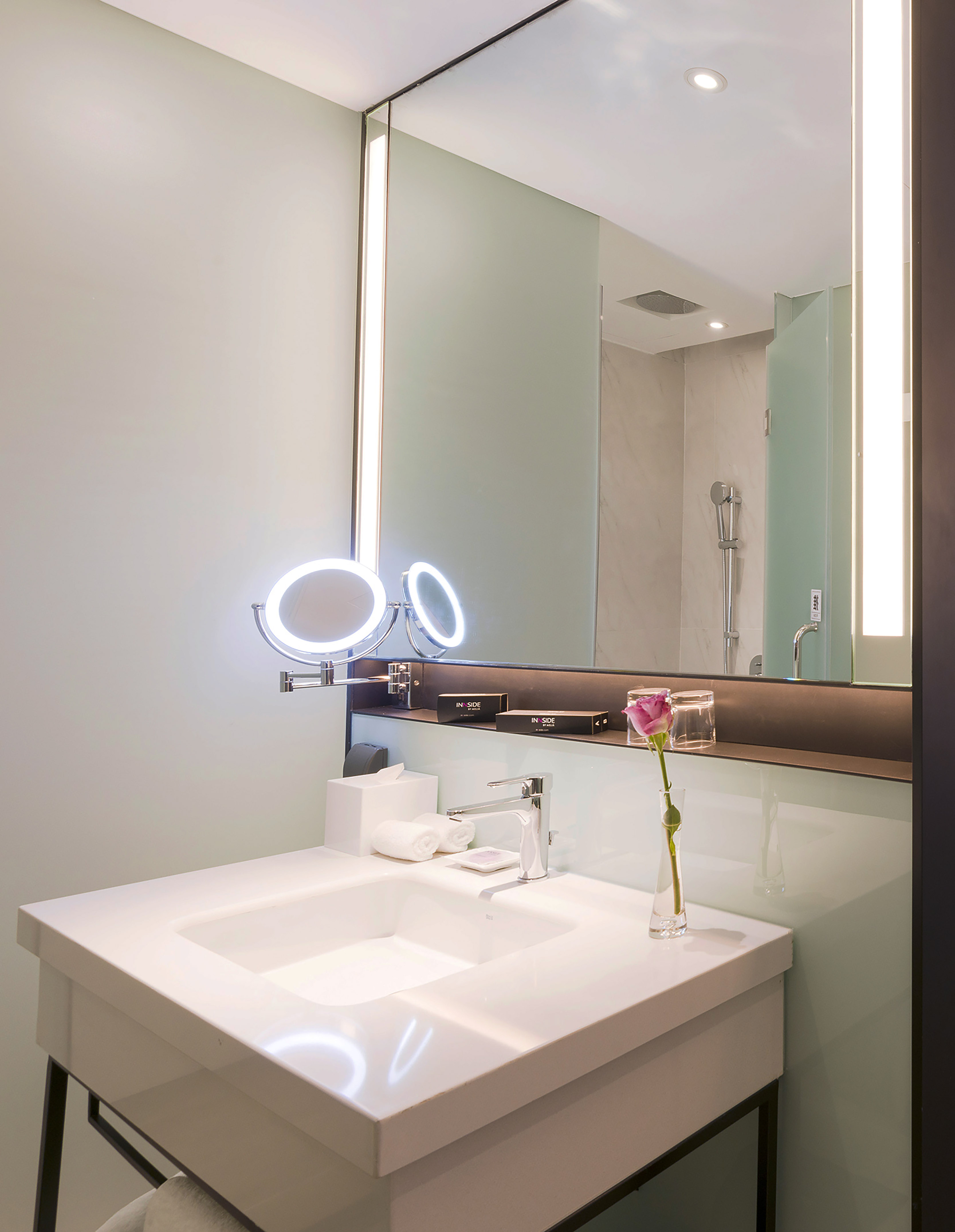 Modern hotel bathroom vanity, lighted mirror, white sink, faucet, rose.