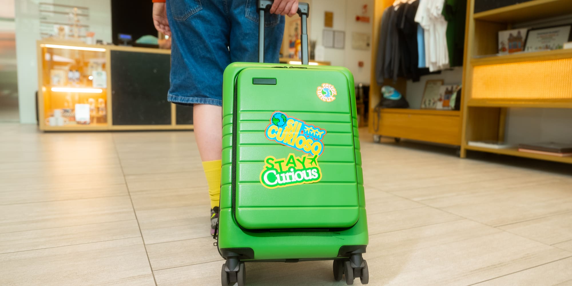 Person pulling bright green travel suitcase with "Stay Curious" stickers.