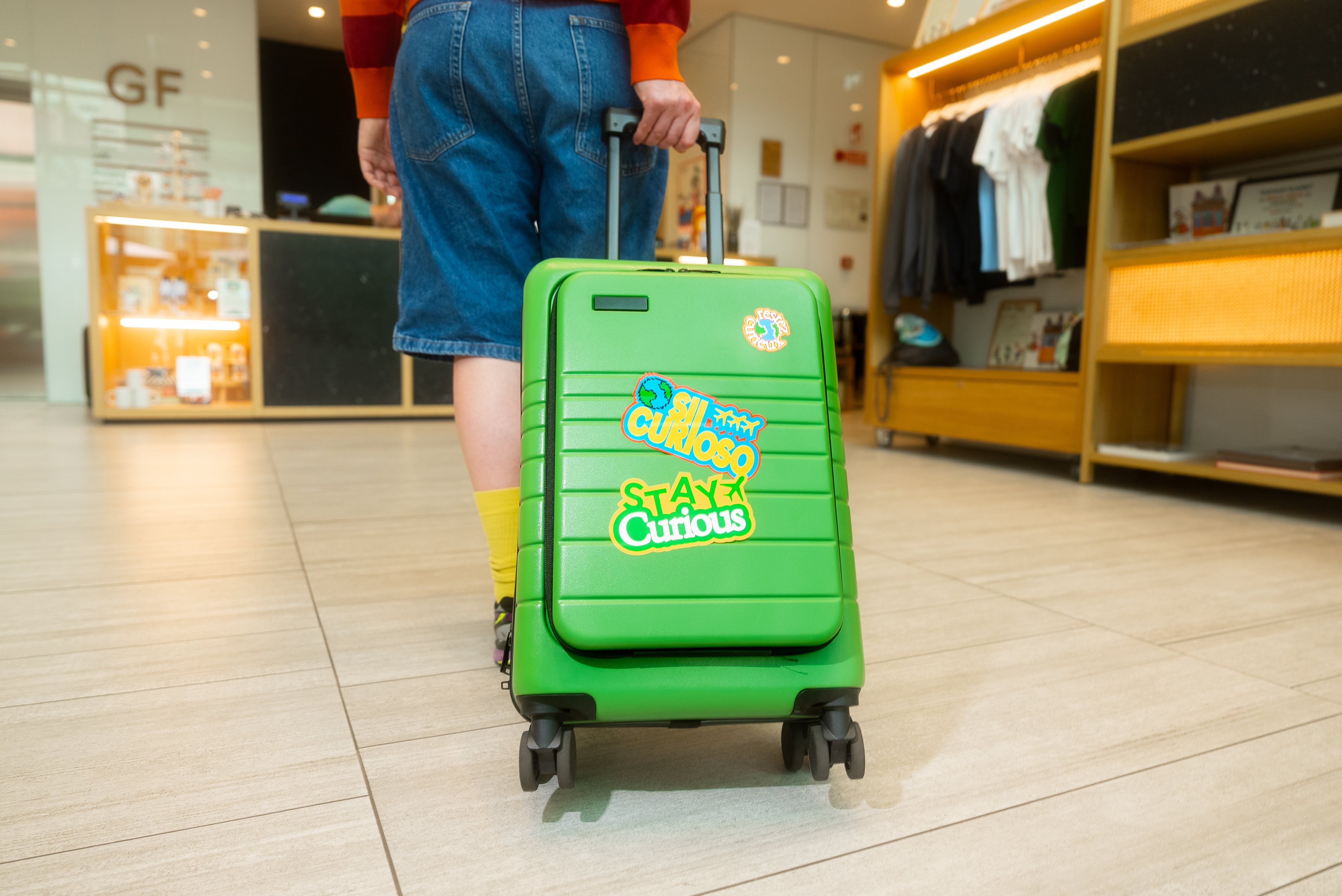 Person pulling bright green travel suitcase with "Stay Curious" stickers.