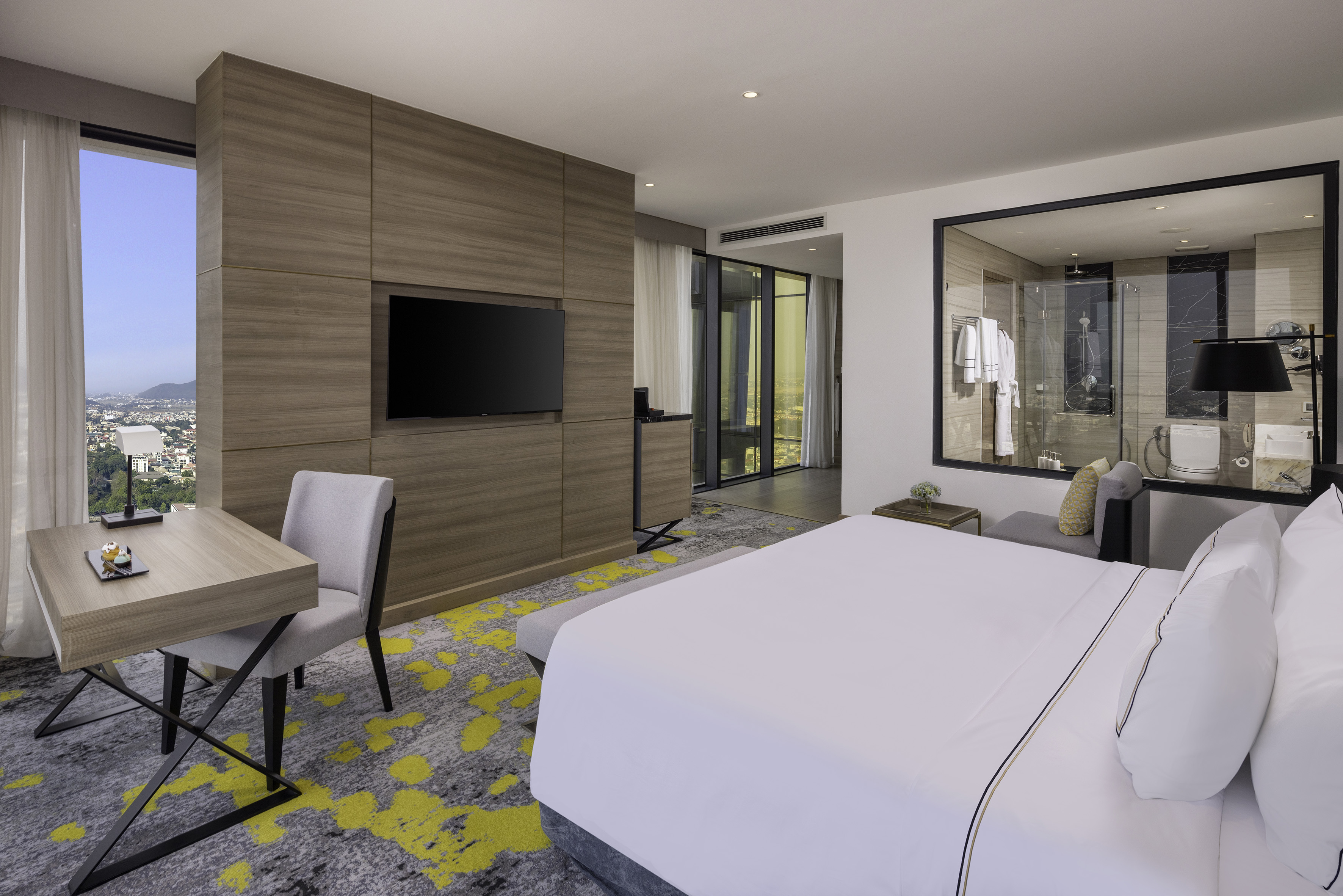 Luxury hotel bedroom with city view, king bed, desk, and modern bathroom.