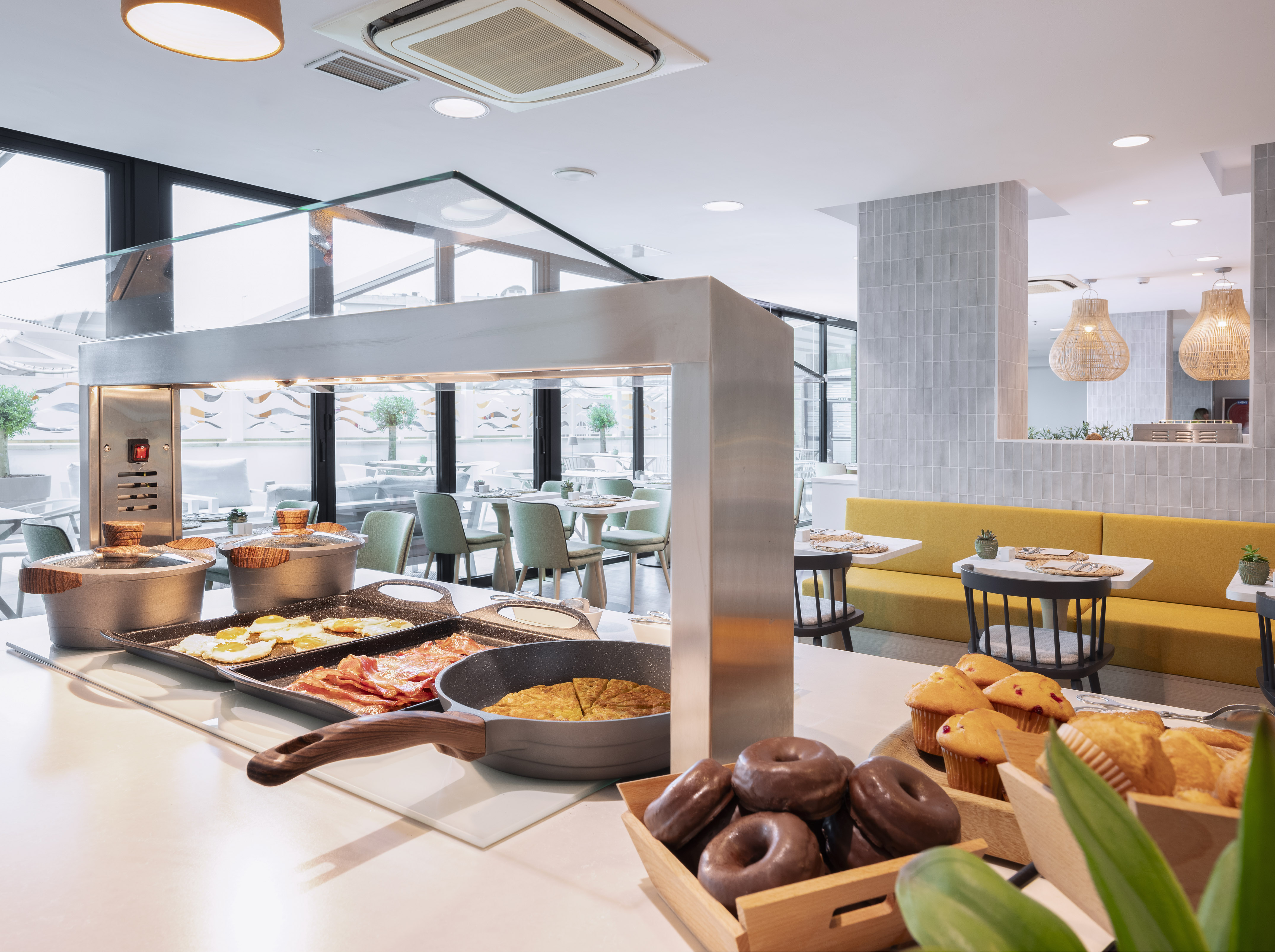 Modern hotel buffet breakfast featuring eggs, bacon, donuts, and muffins.