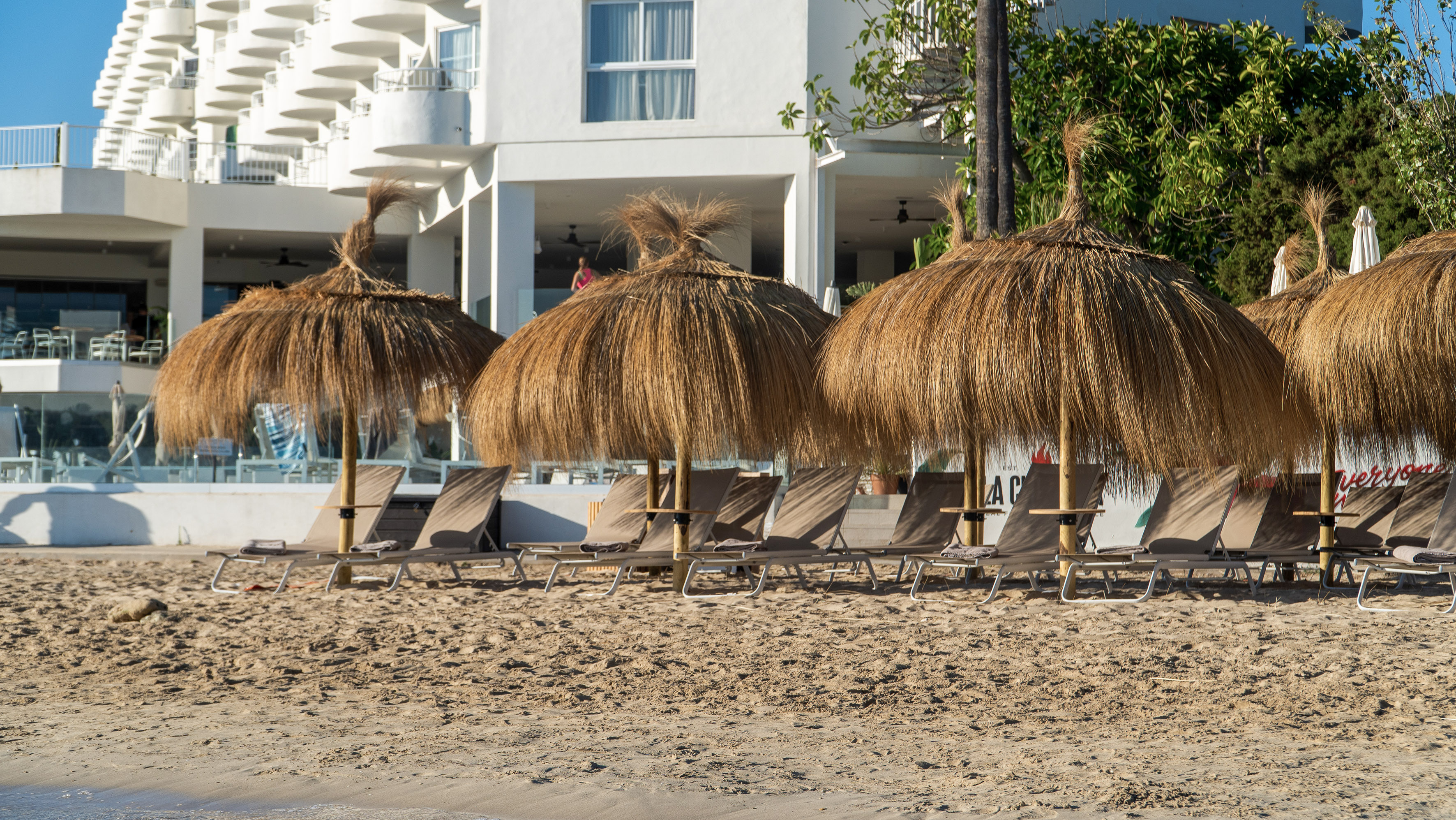 Sandy beach, thatched umbrellas, sun loungers, and hotel resort.