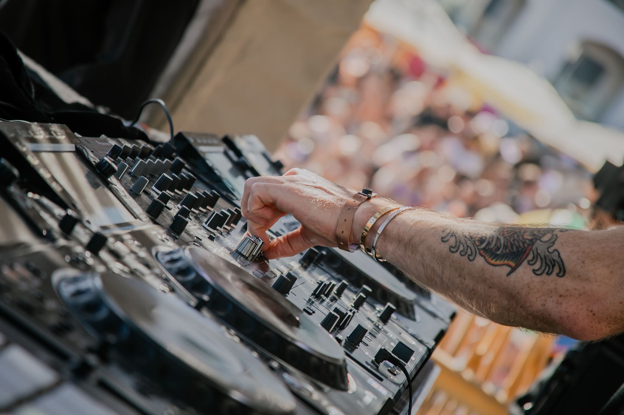 Mano de DJ ajustando mezclador musical en evento con público.